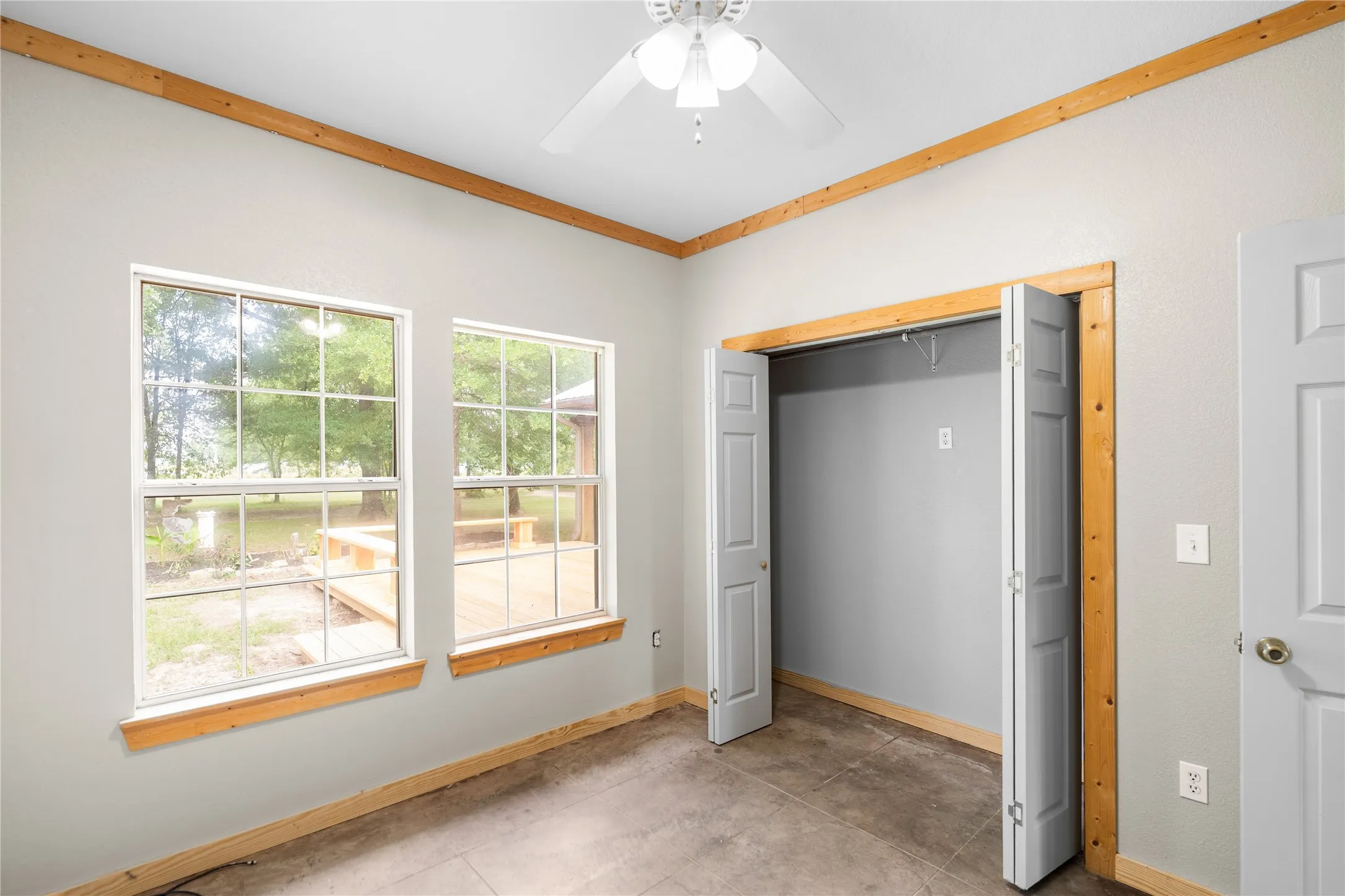 Room featuring wood-finish trim, a ceiling fan, and two windows overlooking a wood deck
