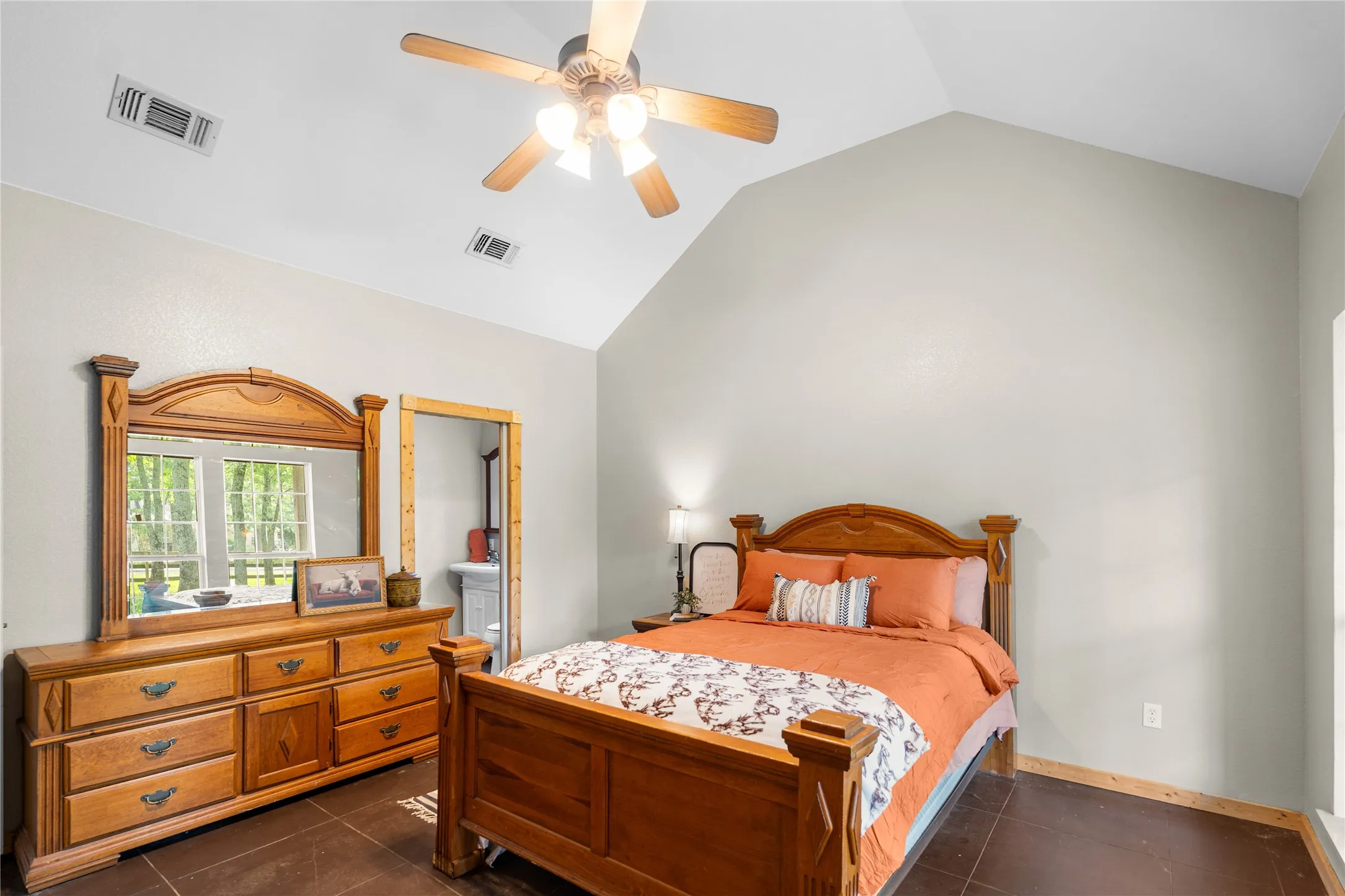 Spacious bedroom featuring vaulted ceilings, a ceiling fan with light kit, and a doorway leading to an adjacent bathroom