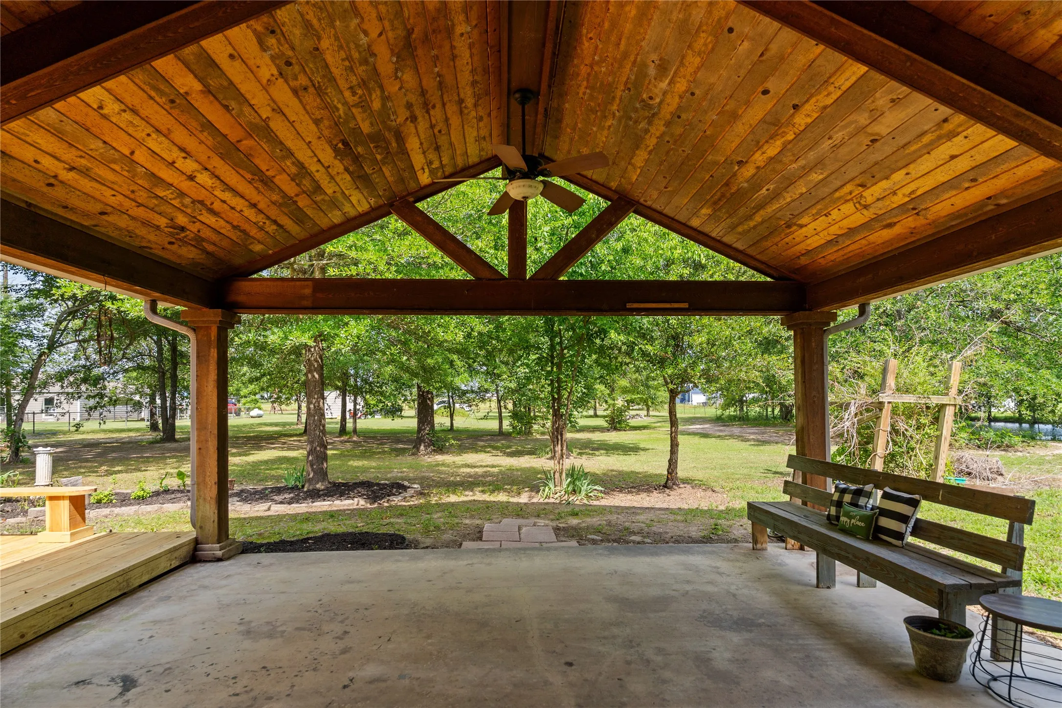 Covered outdoor living area featuring a vaulted wood-plank ceiling, exposed wood beams, and a ceiling fan