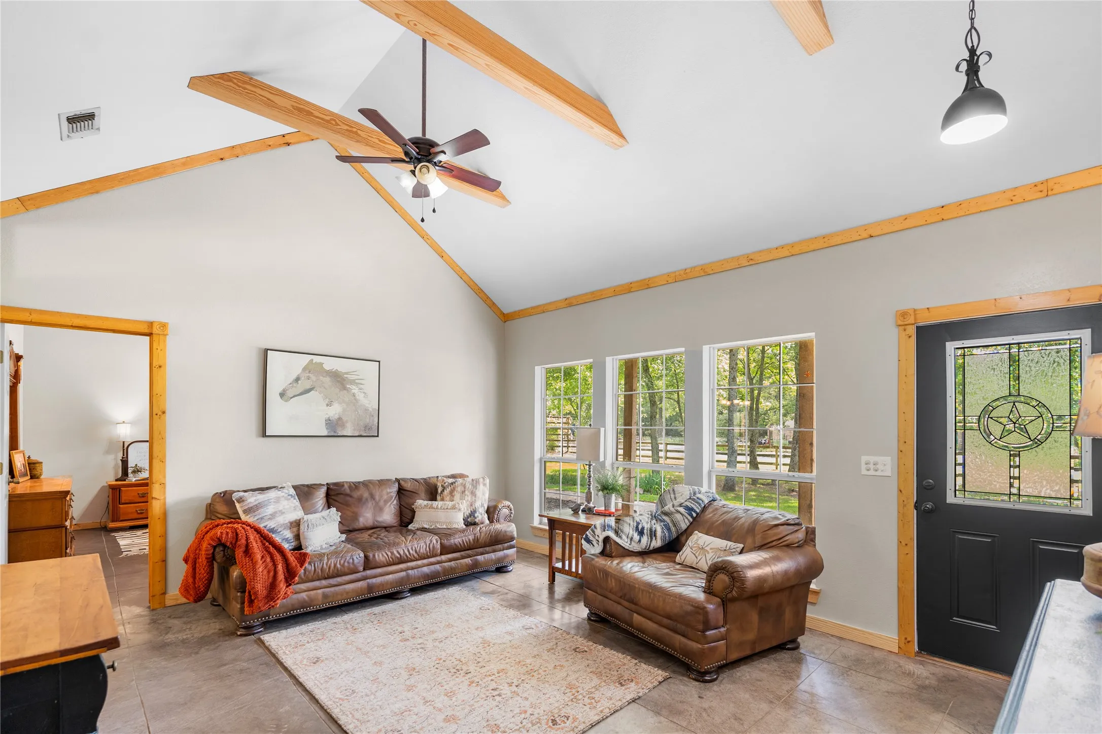 Spacious living area featuring vaulted ceilings with exposed wood beams, a ceiling fan, and concrete flooring