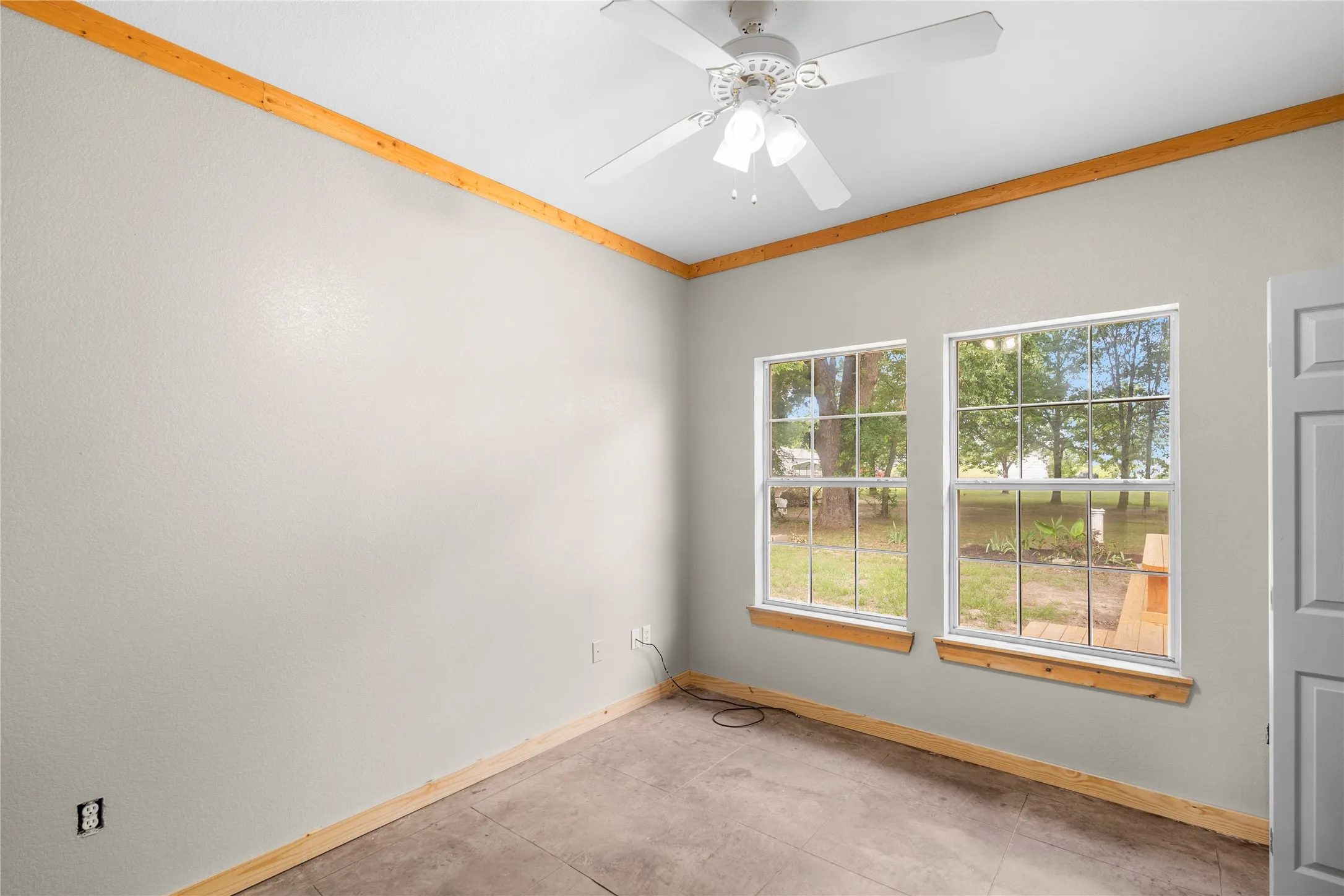 Room featuring neutral wall tones, wood-finish trim, a ceiling fan, and two large windows providing natural light