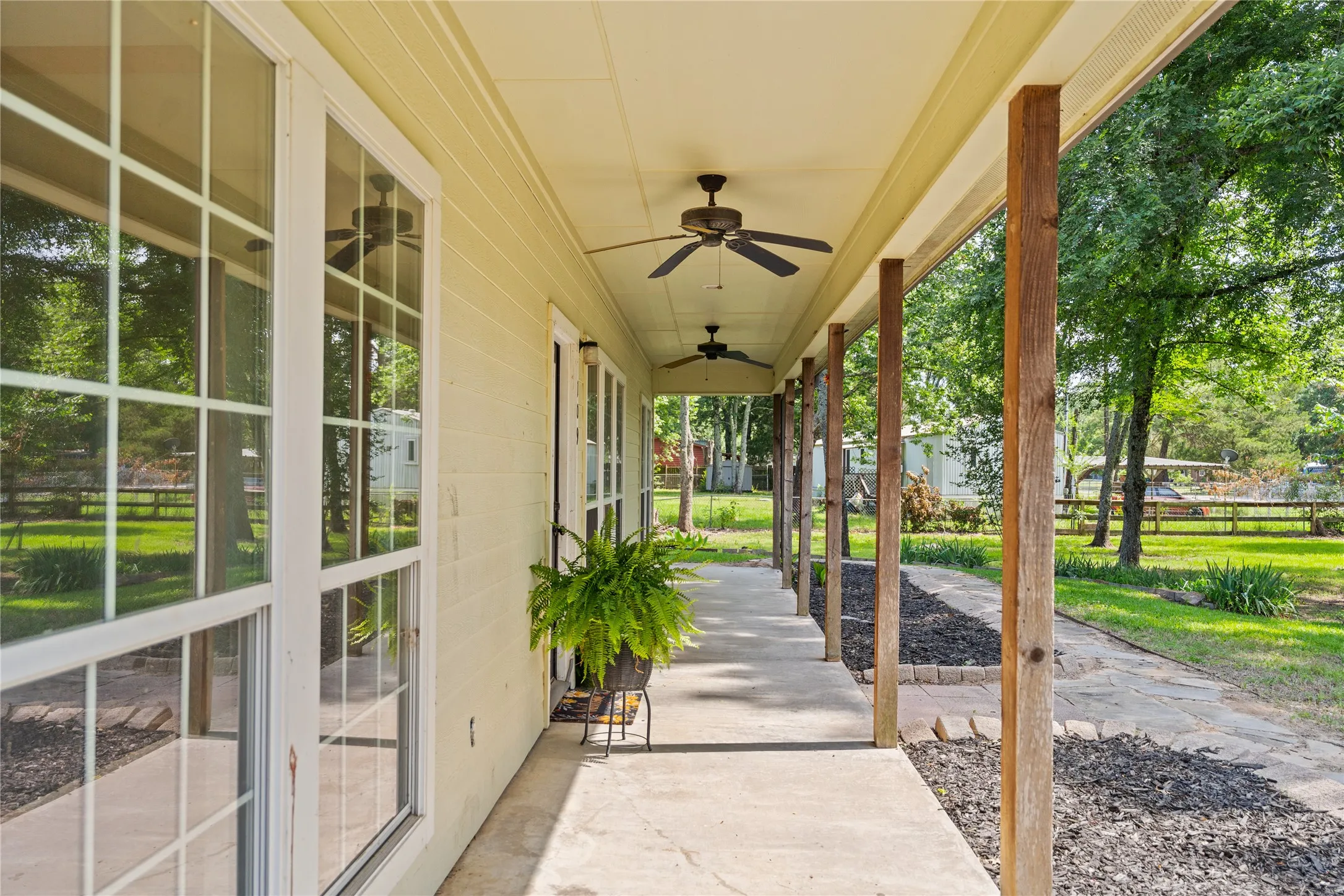 Expansive covered porch featuring a concrete surface, natural wood pillars, multiple ceiling fans, and a stone-edged planting bed