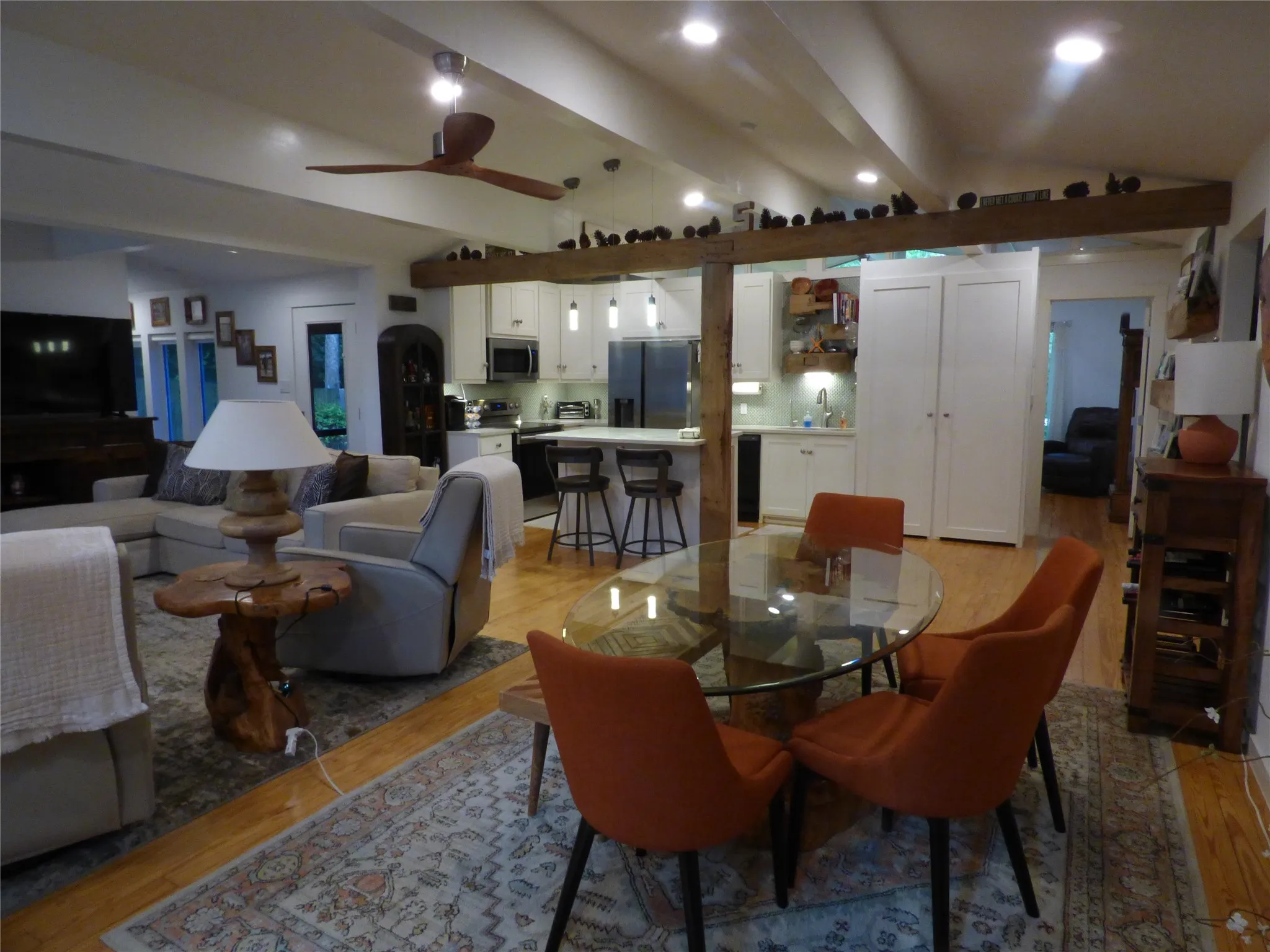 Spacious open-concept living area featuring high vaulted ceilings with exposed beams, wood-finish flooring, recessed lighting, and a kitchen with white cabinetry and an island