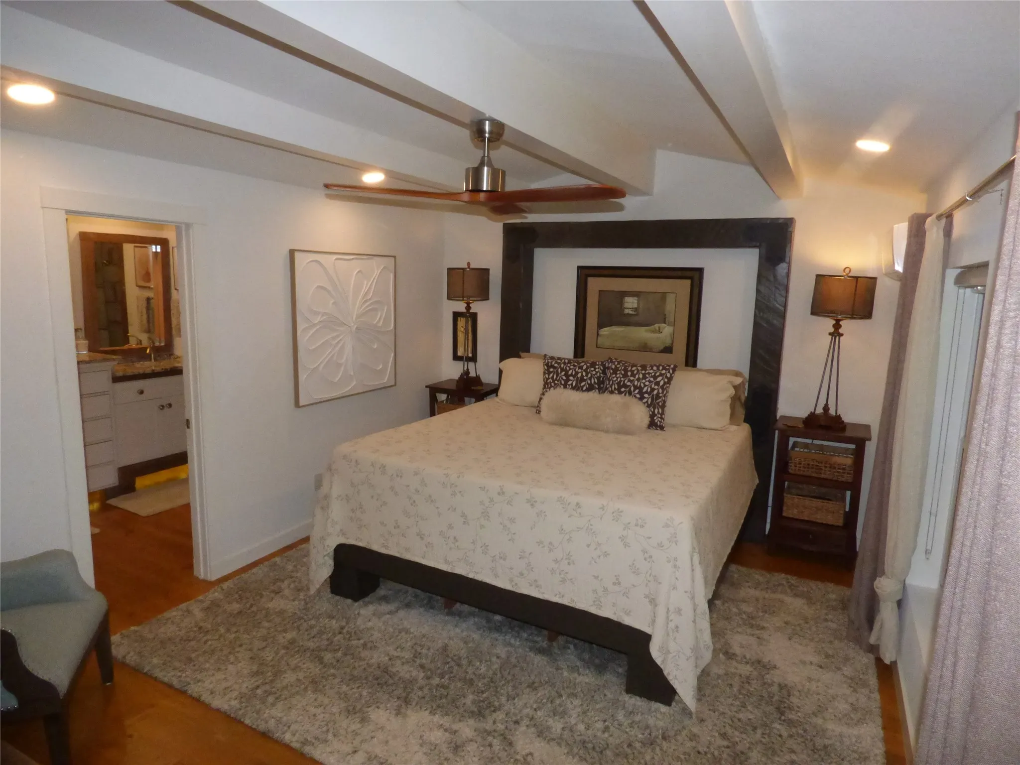 Recessed lighting illuminates the space, featuring a ceiling fan, exposed wood beams, and warm wood-finish flooring