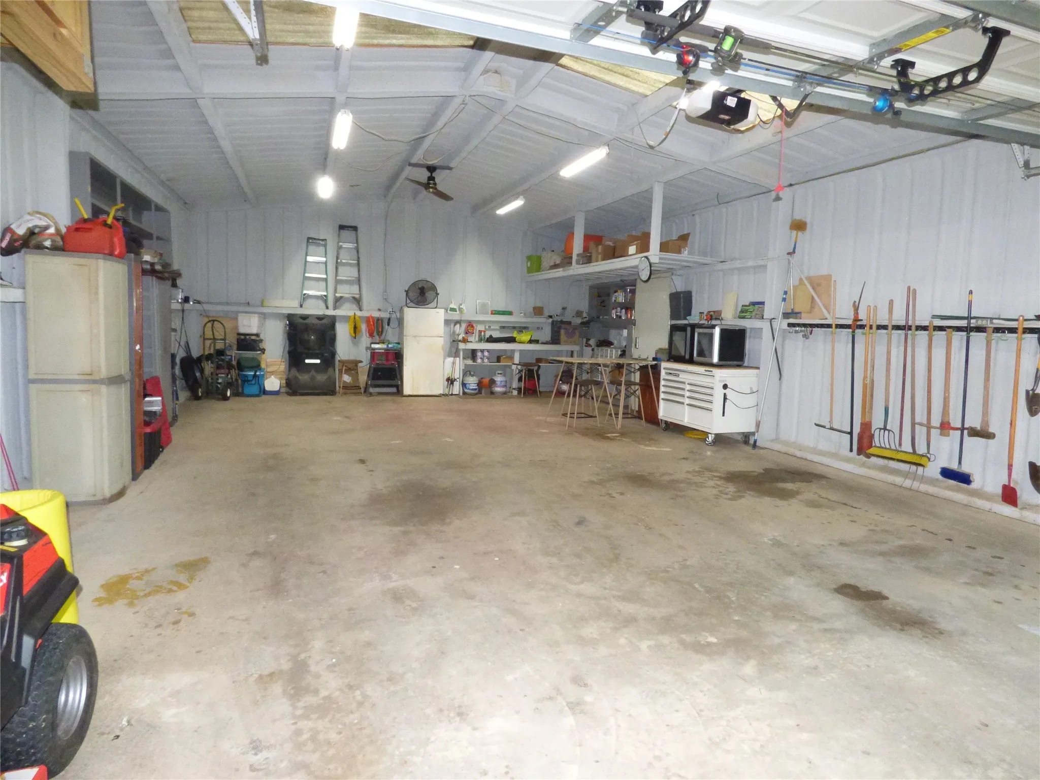Spacious garage with concrete flooring, fluorescent overhead lighting, an exposed metal ceiling, and corrugated metal walls
