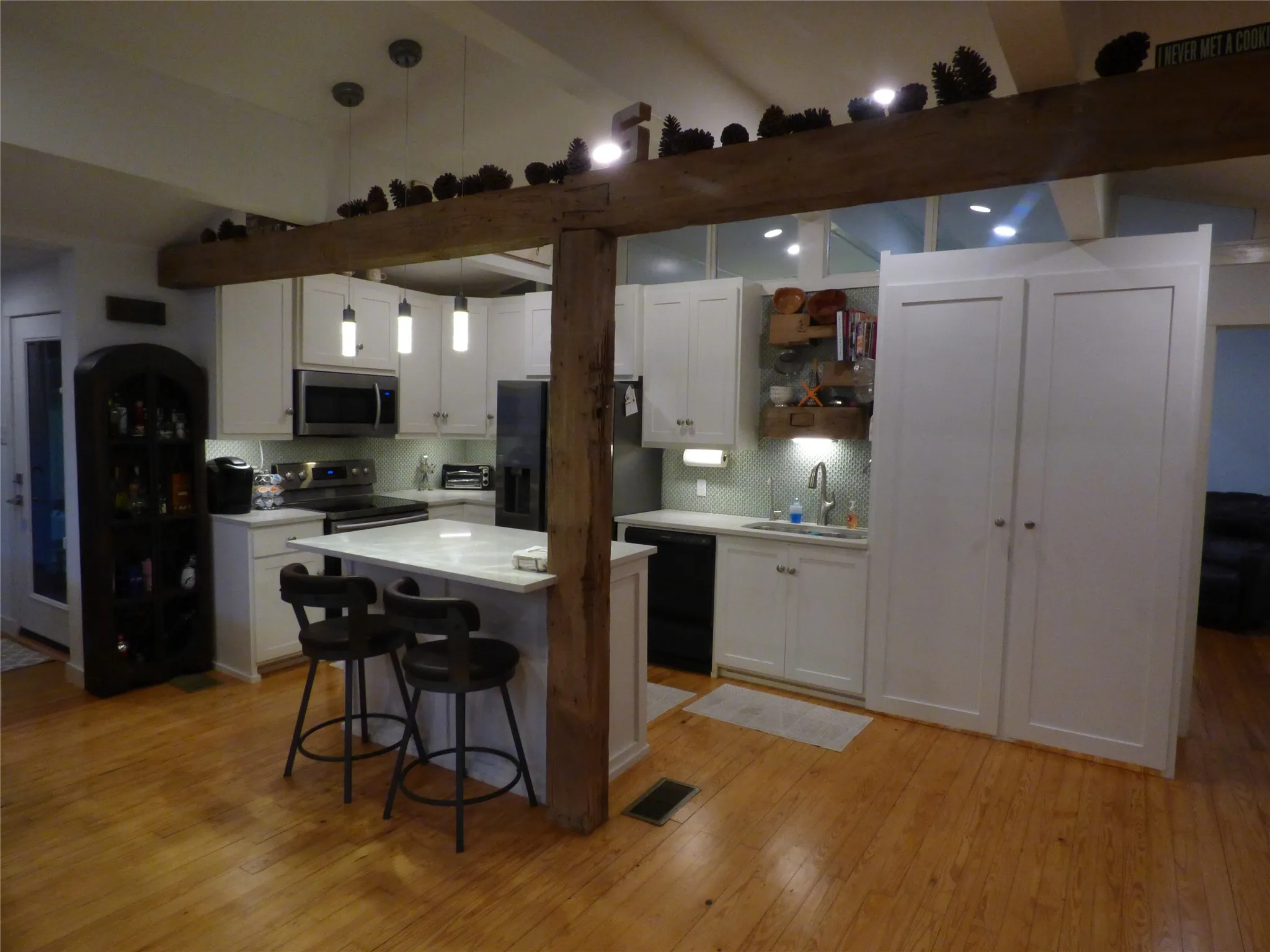 Open-concept kitchen featuring white cabinetry, stainless steel appliances, a central island with a solid surface countertop, wood-finish flooring, and exposed timber beams