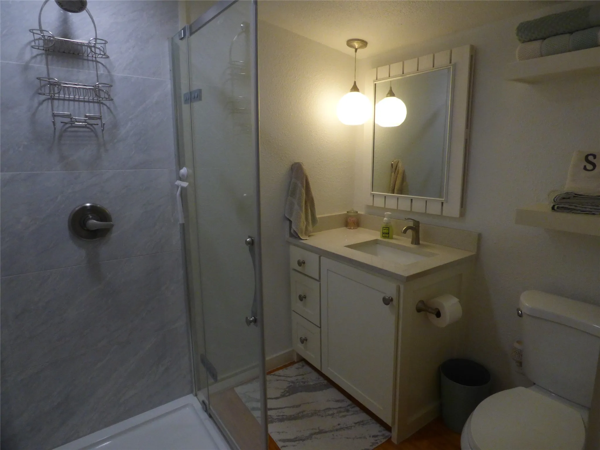 Bathroom featuring a glass-enclosed shower, single vanity with integrated sink, white cabinet storage, light-toned countertop, and a toilet