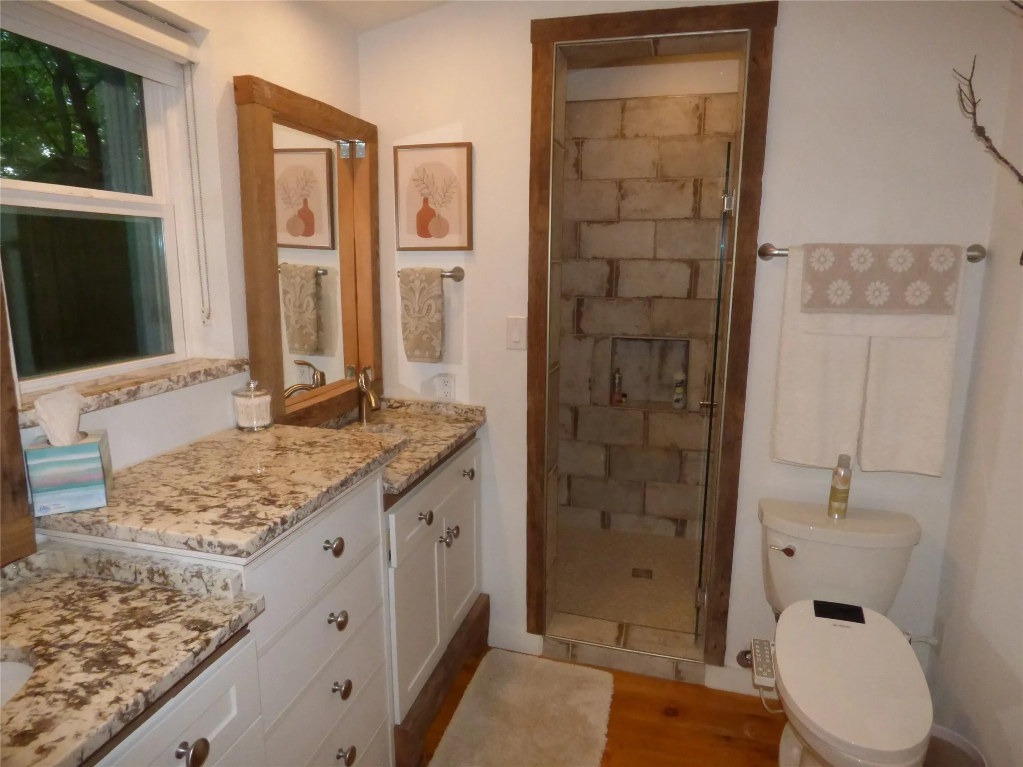 Bathroom featuring a vanity with a multi-toned stone countertop, wood-finish flooring, and a glass-enclosed shower with stone-look wall tiles
