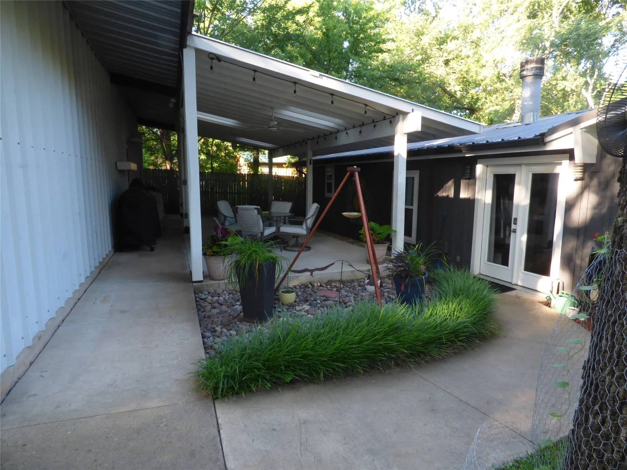Expansive concrete patio area features a covered outdoor living space with string lighting and a ceiling fan