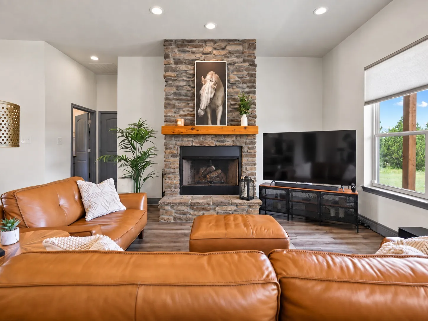 Stone-clad fireplace with a wood mantle, recessed lighting, wood-finish flooring, and a large window