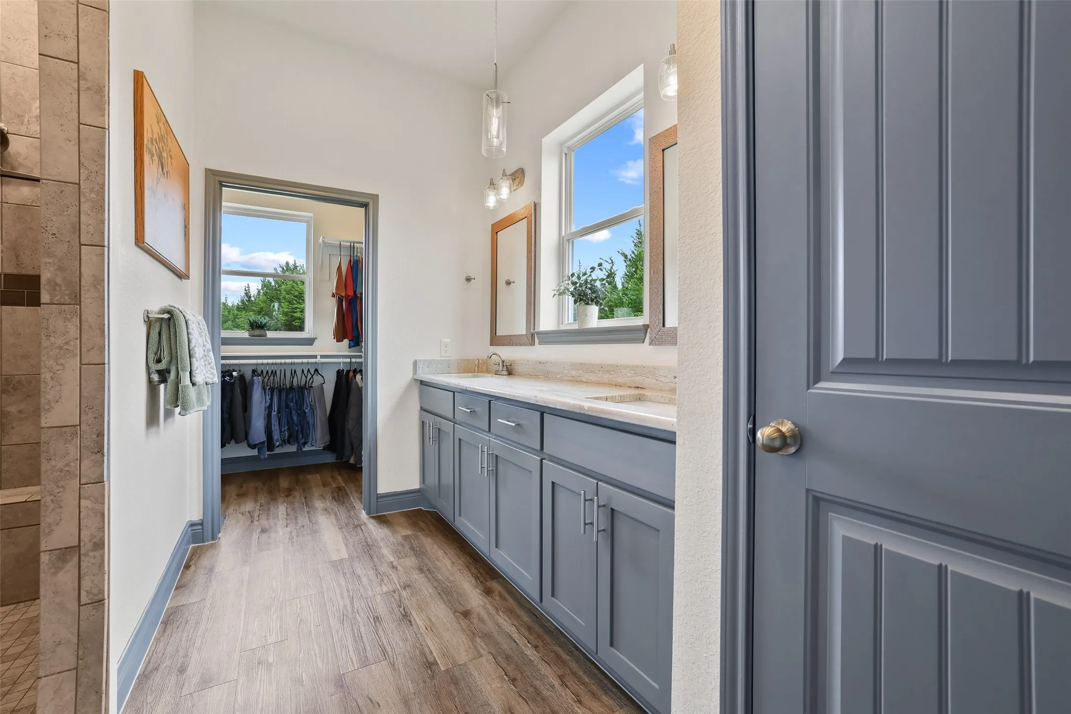 Bathroom featuring a double vanity with light-colored countertops, wood-finish flooring, and a walk-in closet with a window