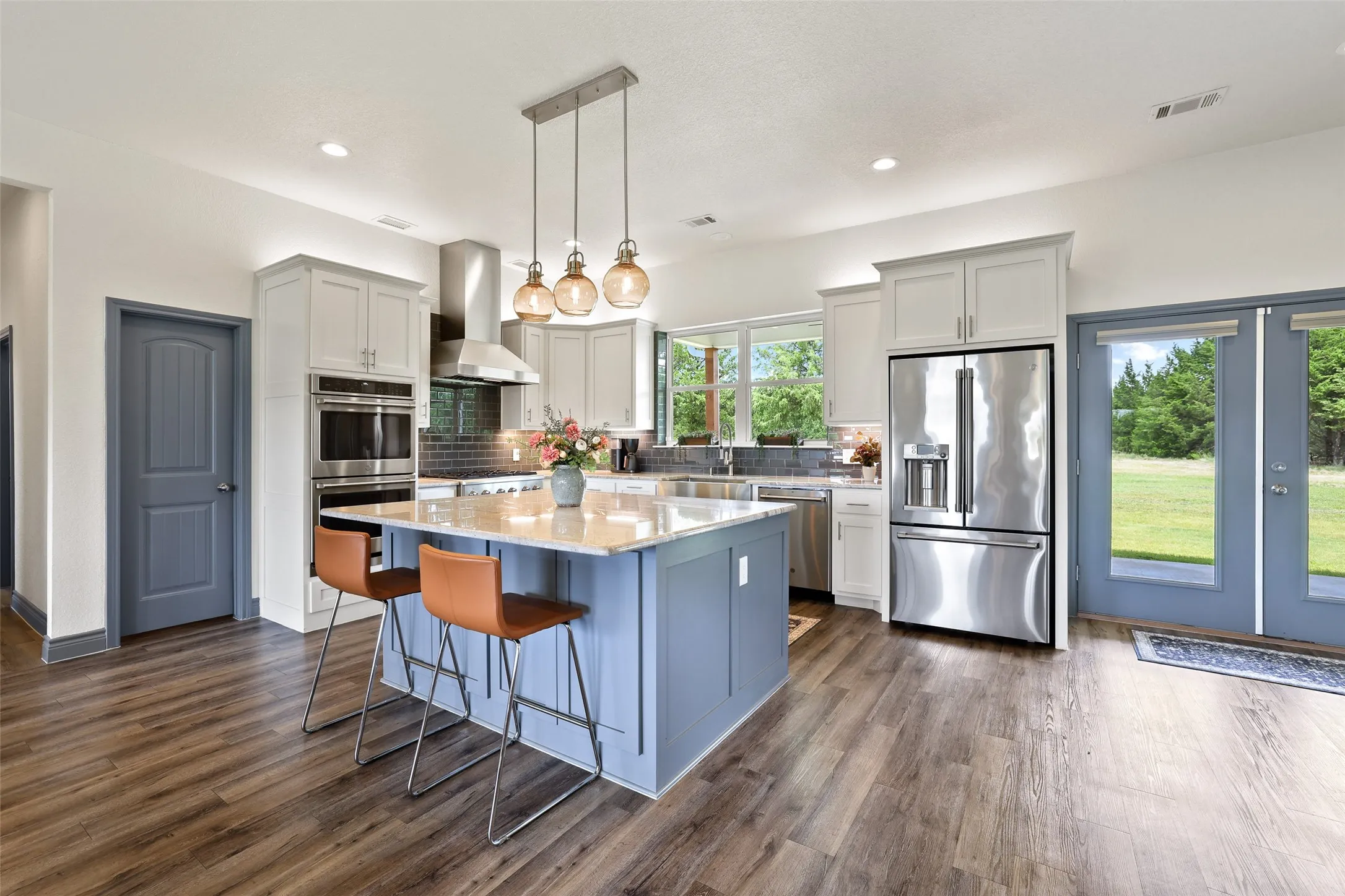 Gourmet kitchen featuring a large central island with light-toned countertop, stainless steel appliances, wood-finish flooring, recessed lighting, and direct access to the outdoor space
