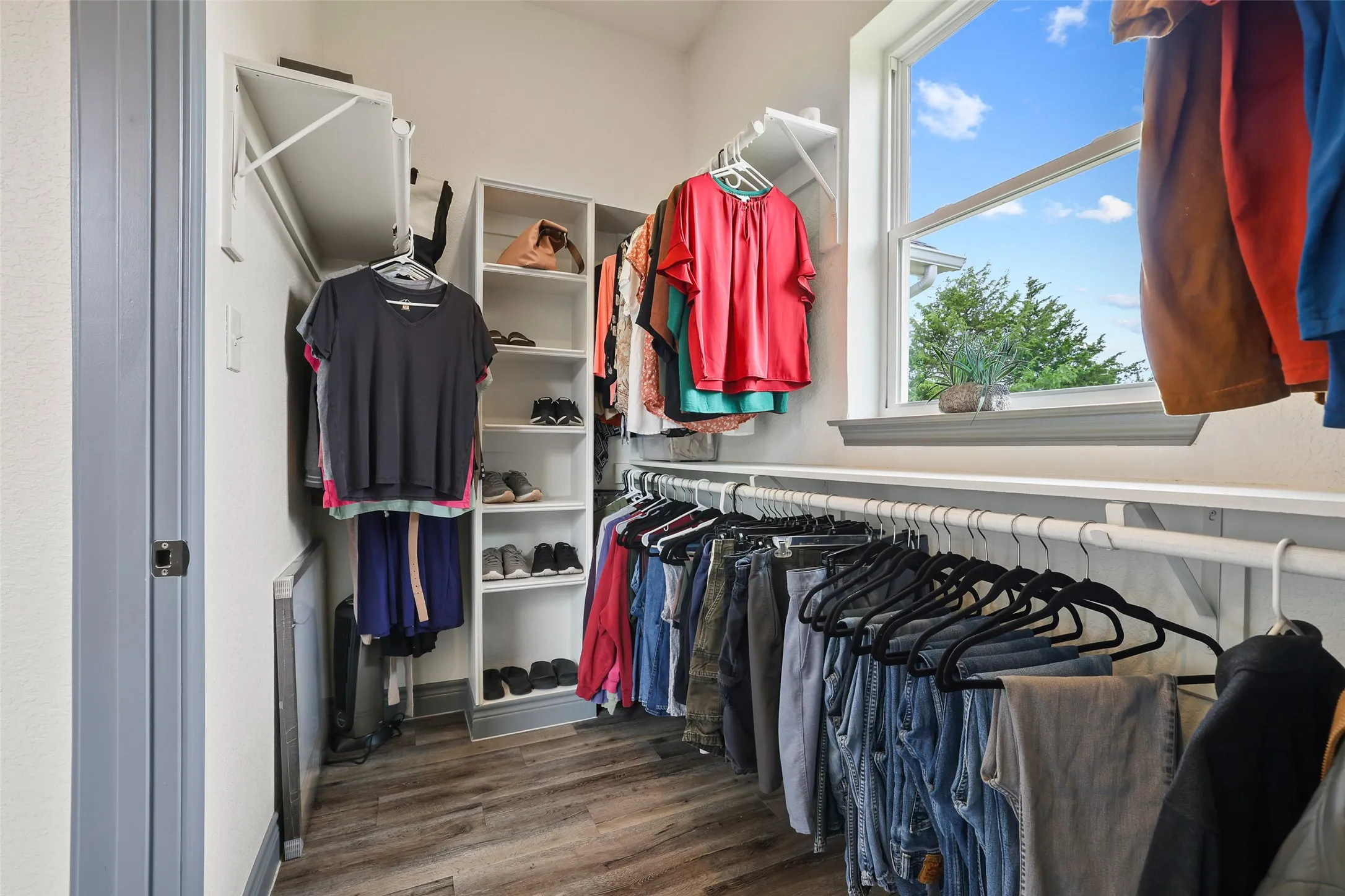 Custom closet system featuring wood-finish flooring, built-in shelving, ample hanging rods, and a window with natural light