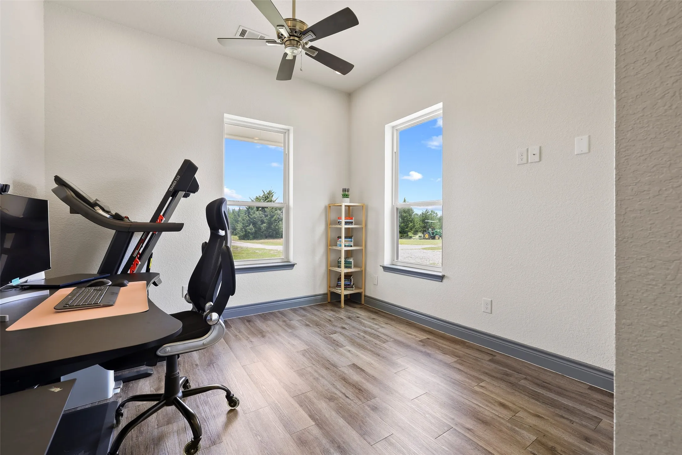 Room featuring wood-finish flooring, two large windows, a ceiling fan, and light-toned walls