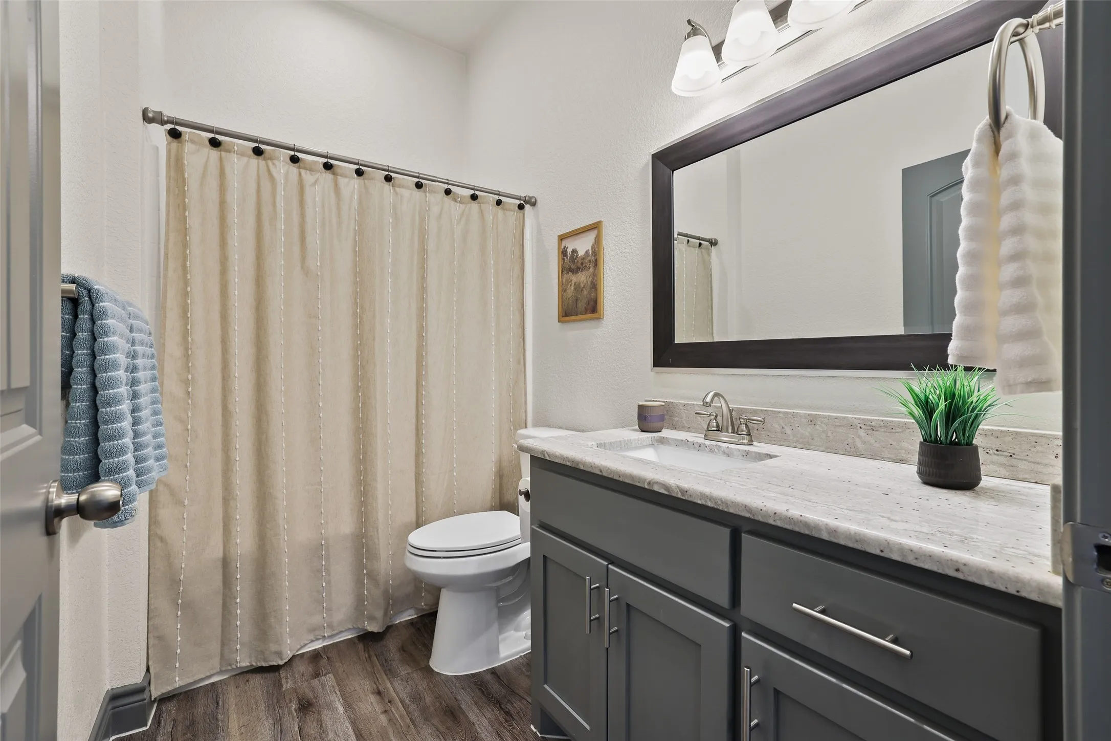 Full bathroom featuring a single vanity with gray cabinetry, a light-toned countertop, and a framed mirror with overhead lighting
