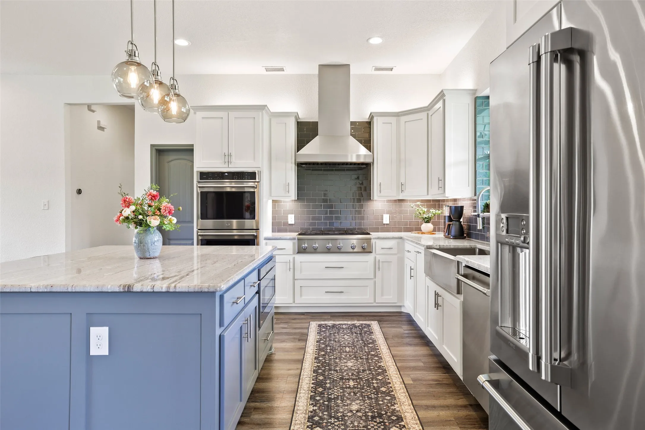 Gourmet kitchen featuring a substantial island with stone countertop, stainless steel appliances, white cabinetry, and a dark tile backsplash