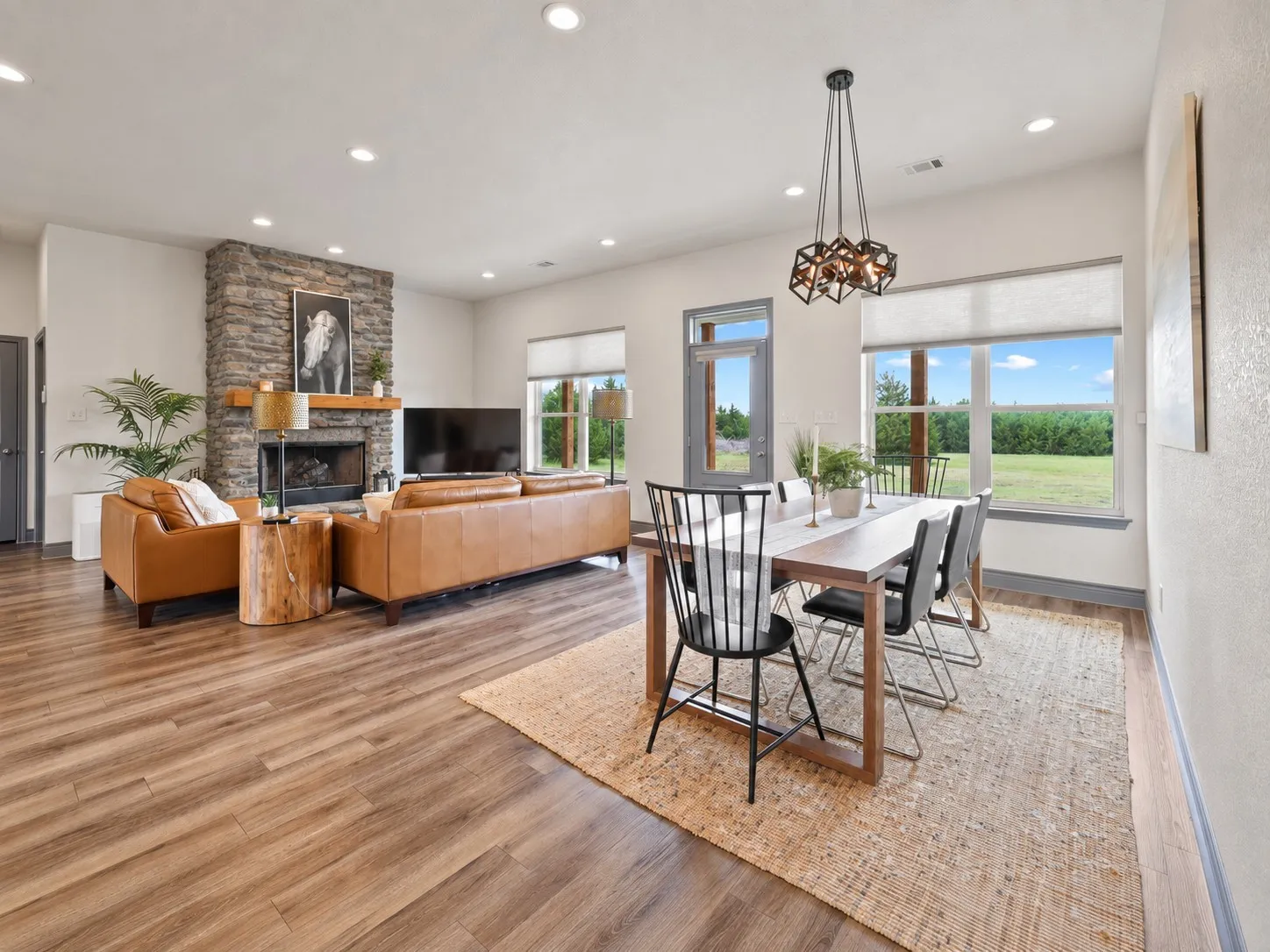 Open-concept living area featuring wood-finish flooring, a stone fireplace with a wood mantle, recessed lighting, and a modern dining chandelier