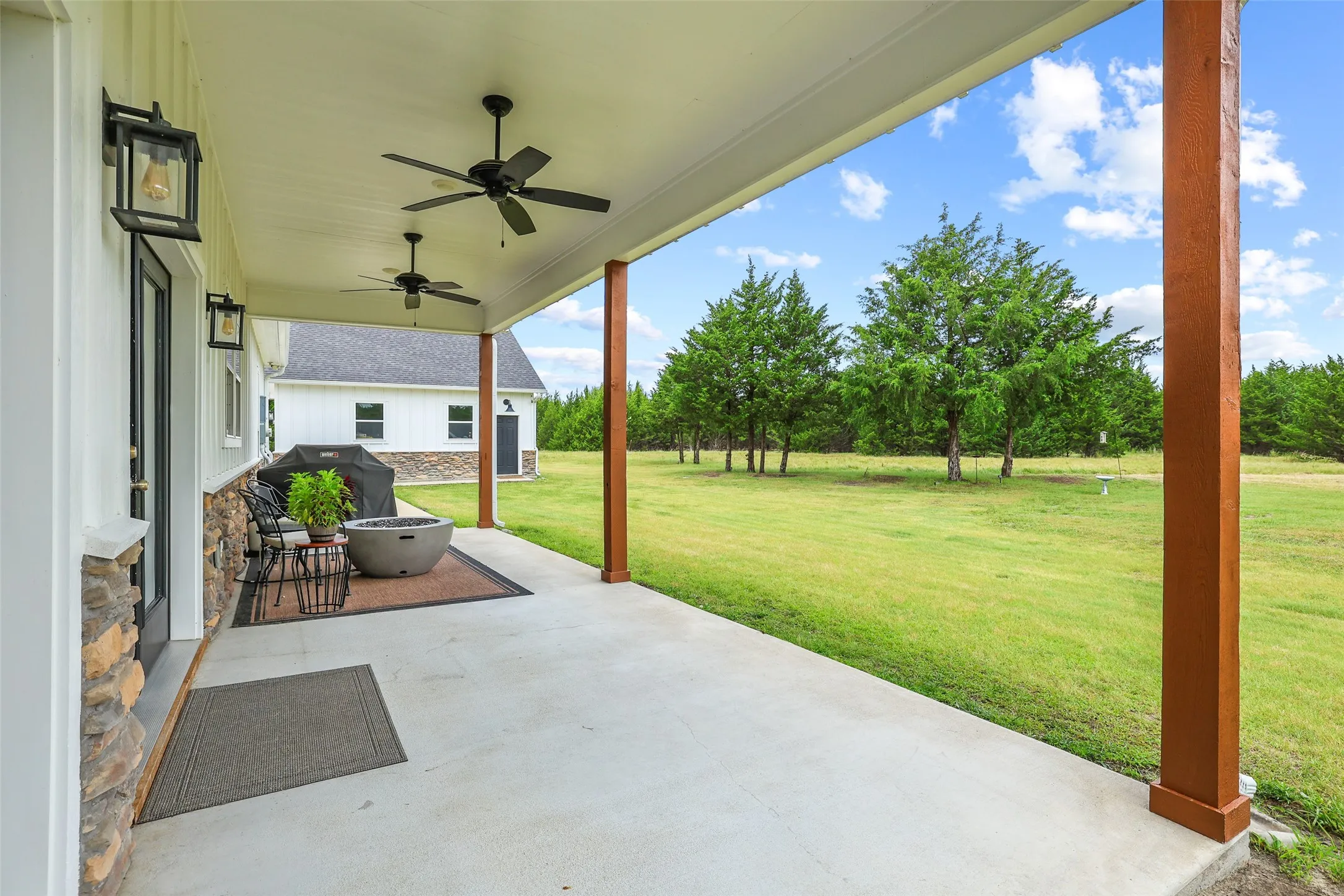 Spacious covered patio featuring concrete flooring, exposed wood support beams, and two ceiling fans