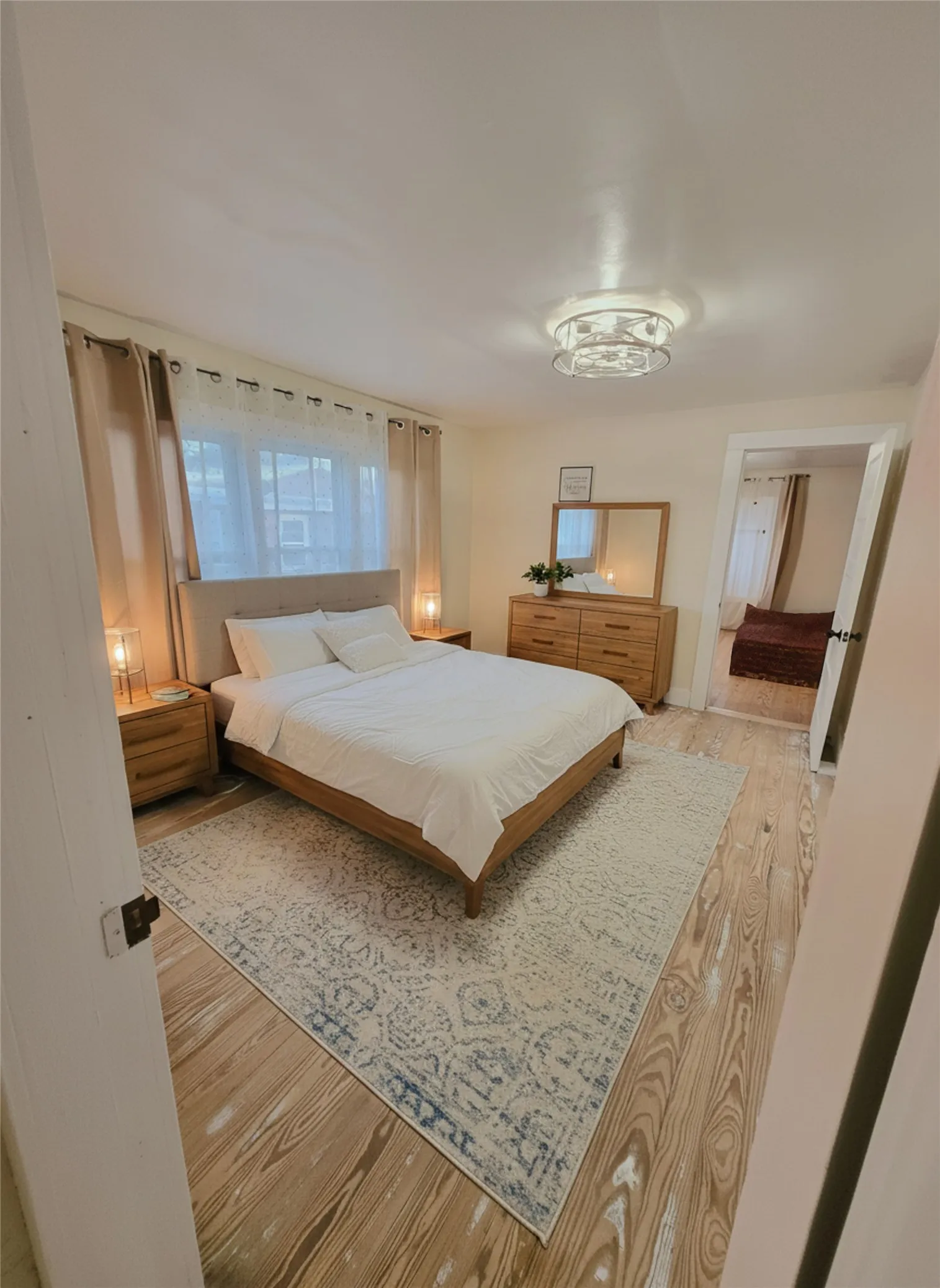 Natural light illuminates this tranquil bedroom featuring rich hardwood flooring and a stylish overhead fixture. DIGITAL STAGING