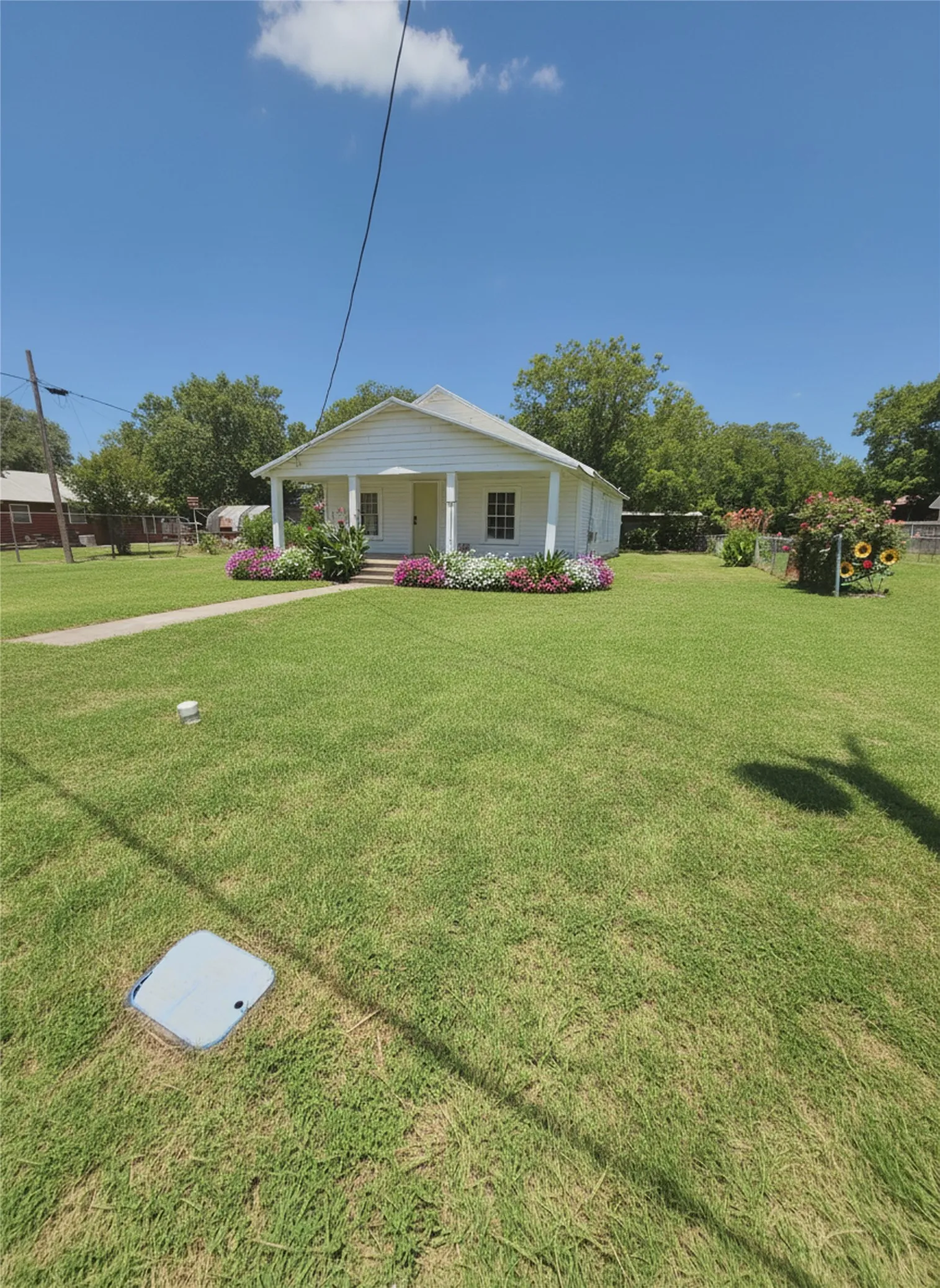 A charming single-story home with a welcoming front porch and vibrant flower beds. DIGITAL STAGING