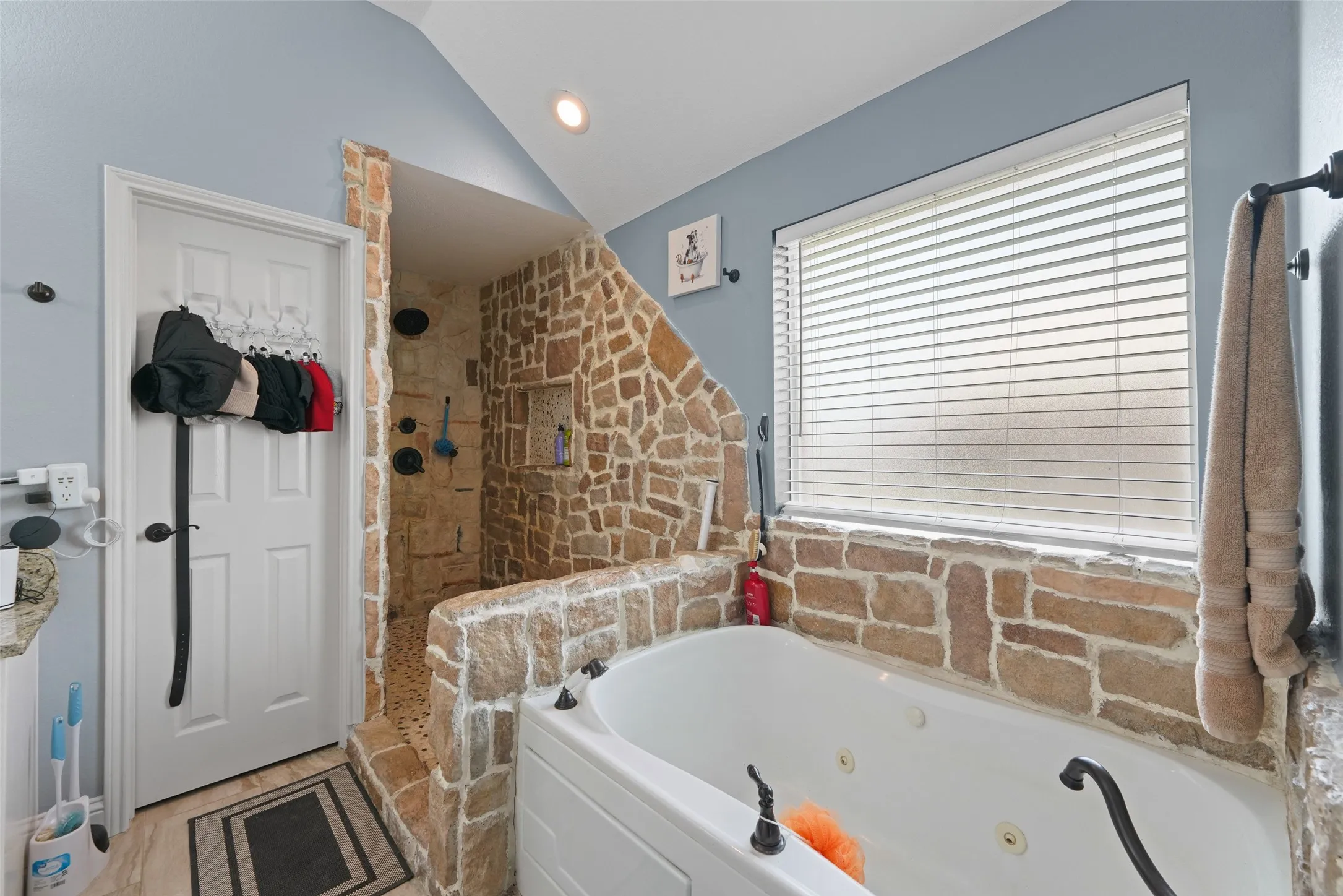 Stone-clad walk-in shower with integrated niche and jetted soaking tub create a spa-like bathroom experience