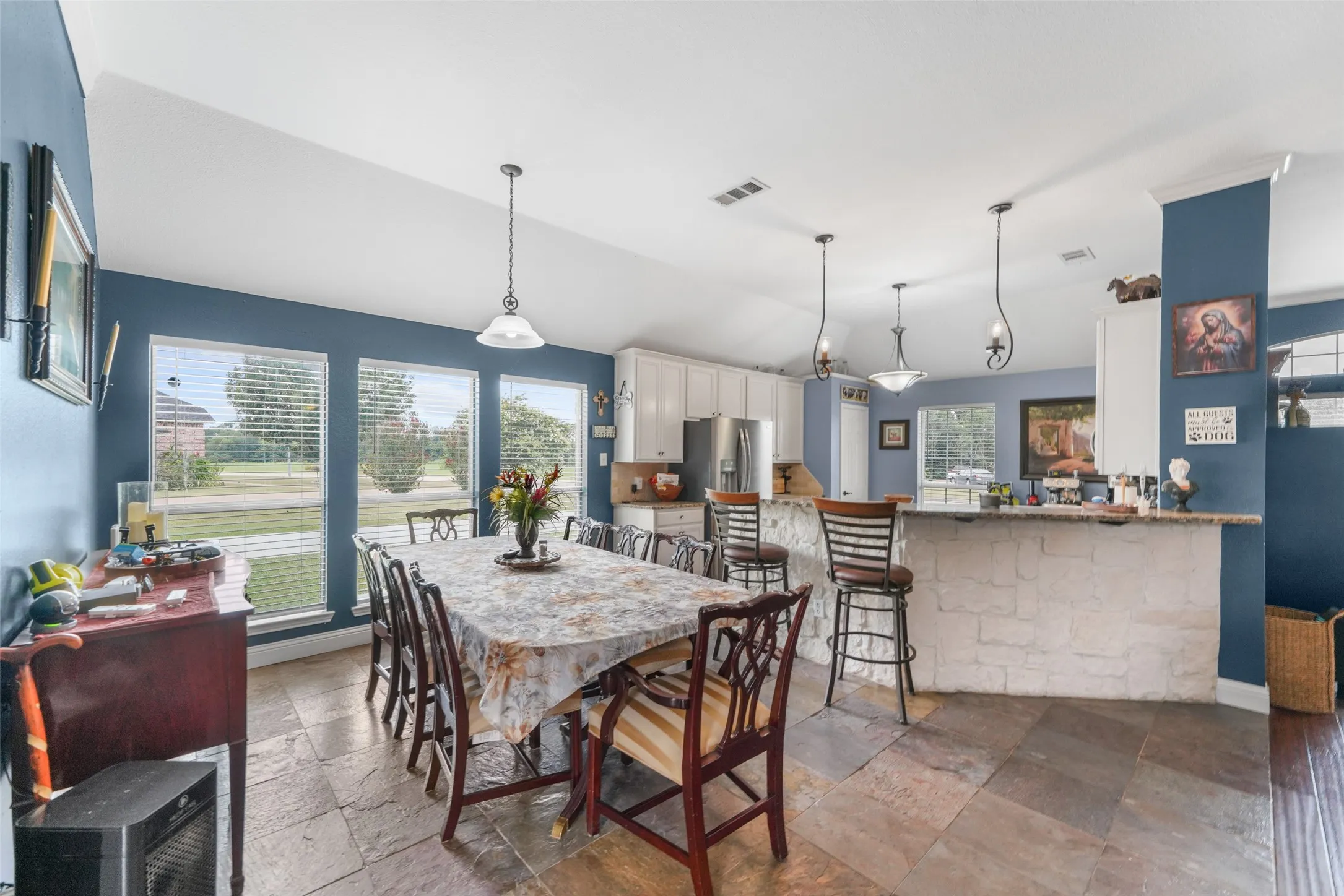 Expansive open-concept living space featuring vaulted ceilings, slate-tile flooring, and multiple windows