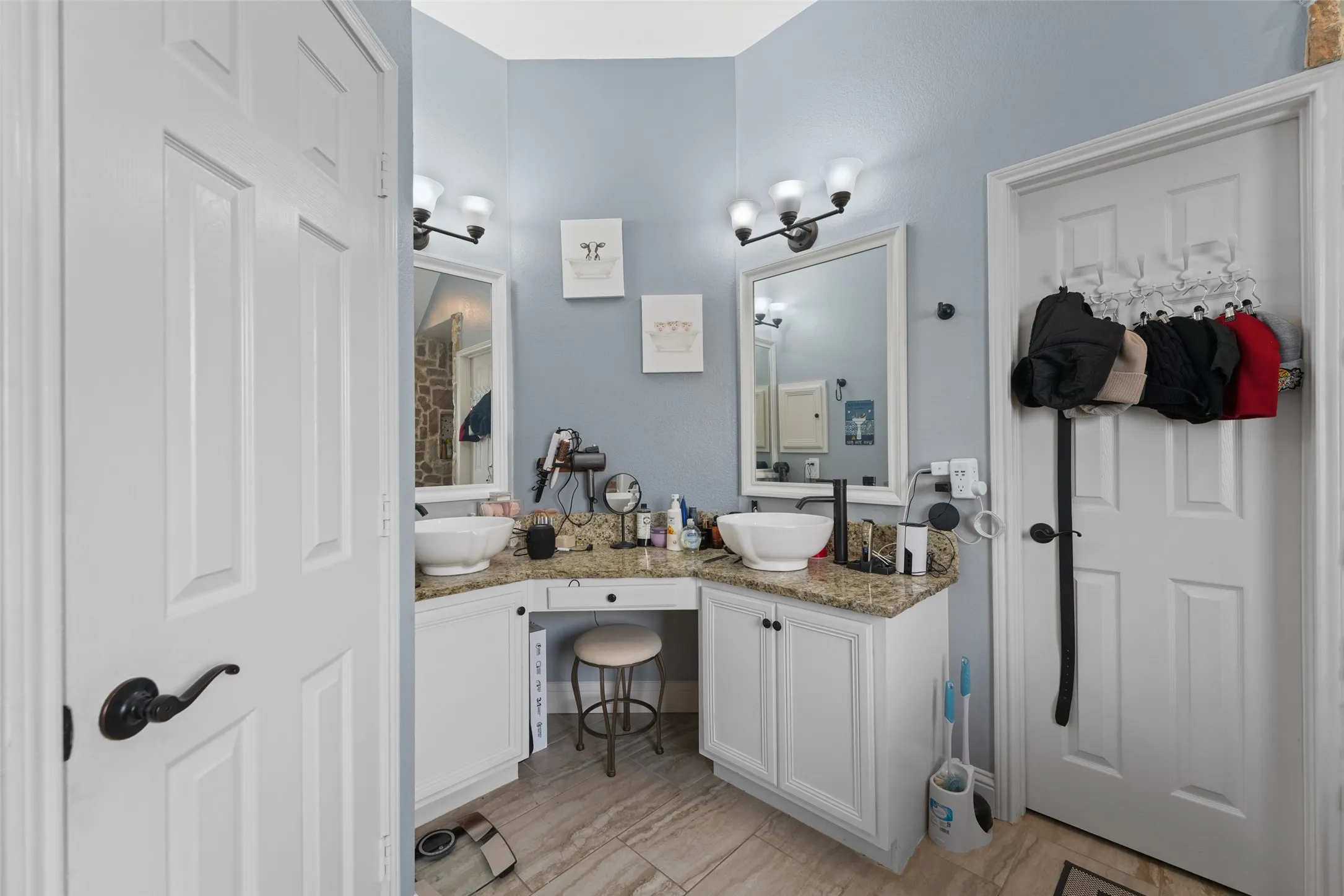 Dual vanity with granite countertops, vessel sinks, white cabinetry, and wood-finish tile flooring
