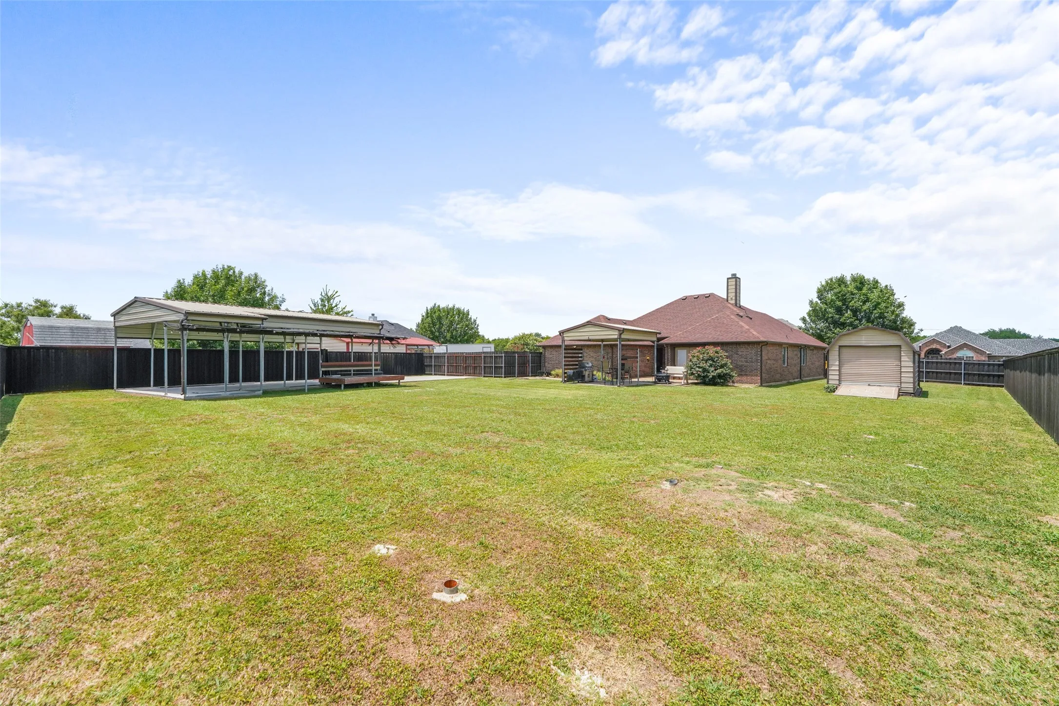 Expansive backyard with a large metal carport featuring an attached wood deck
