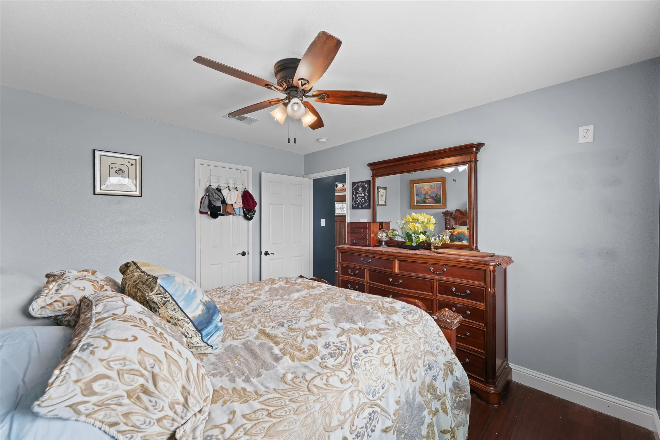 Bedroom featuring light gray walls, dark wood-finish flooring, a ceiling fan with light kit, and white paneled doors