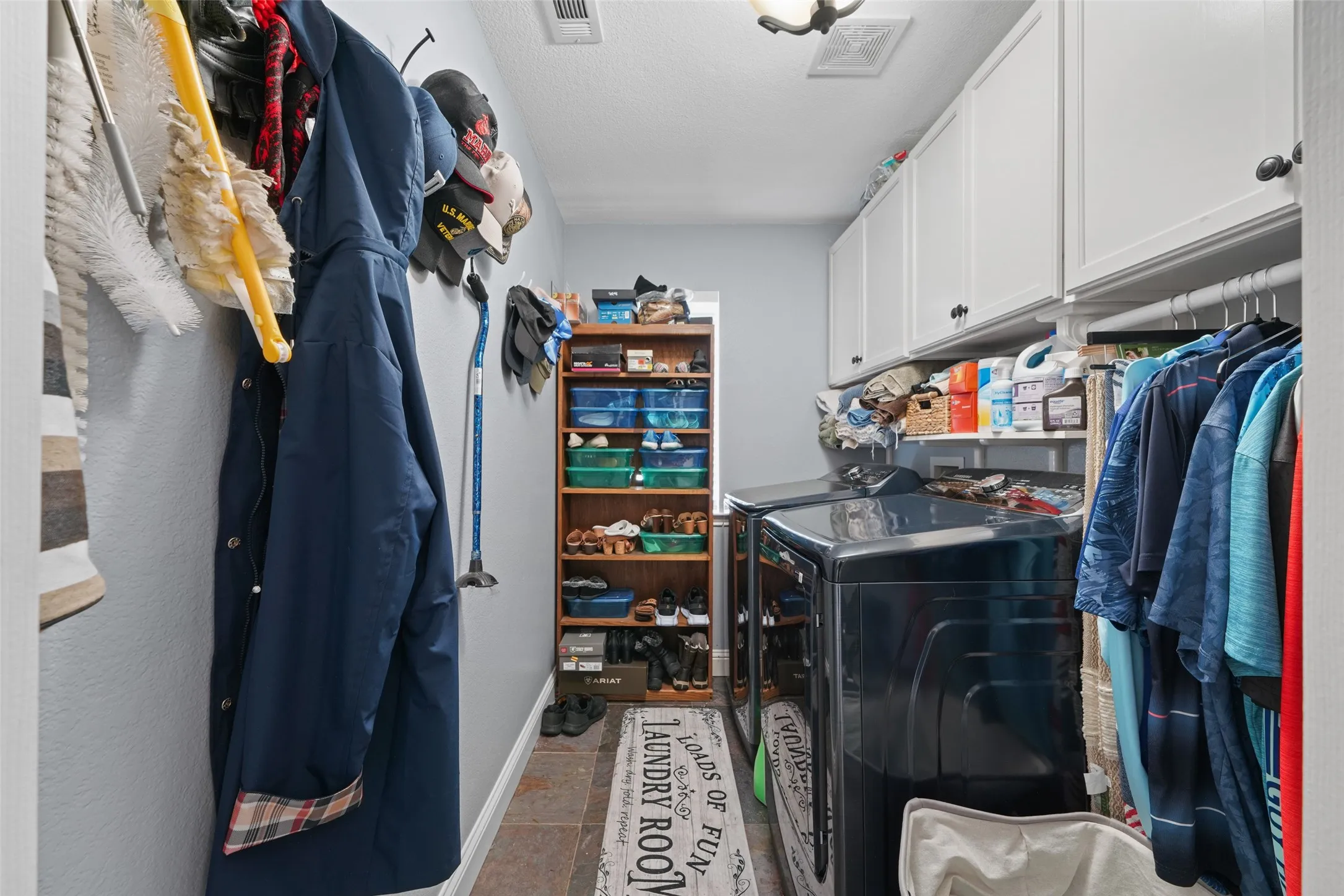 Dedicated laundry area featuring white upper cabinetry, tiled flooring, built-in shelving, and a clothing rod