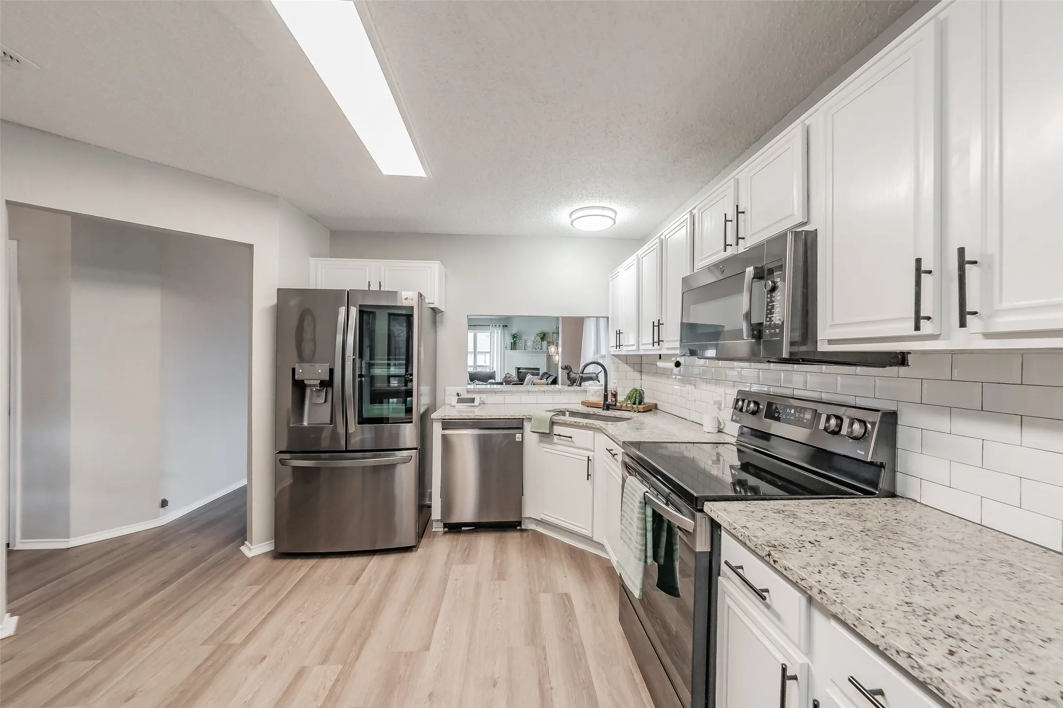 Contemporary kitchen featuring, white cabinetry with black hardware, stainless steel appliances, granite countertops, and a white subway tile backsplash