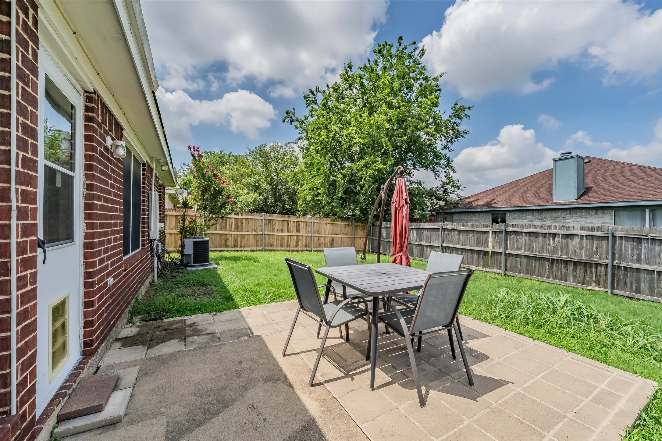 Expansive backyard featuring a red brick exterior, a stone patio, a wooden privacy fence, and a mature trees