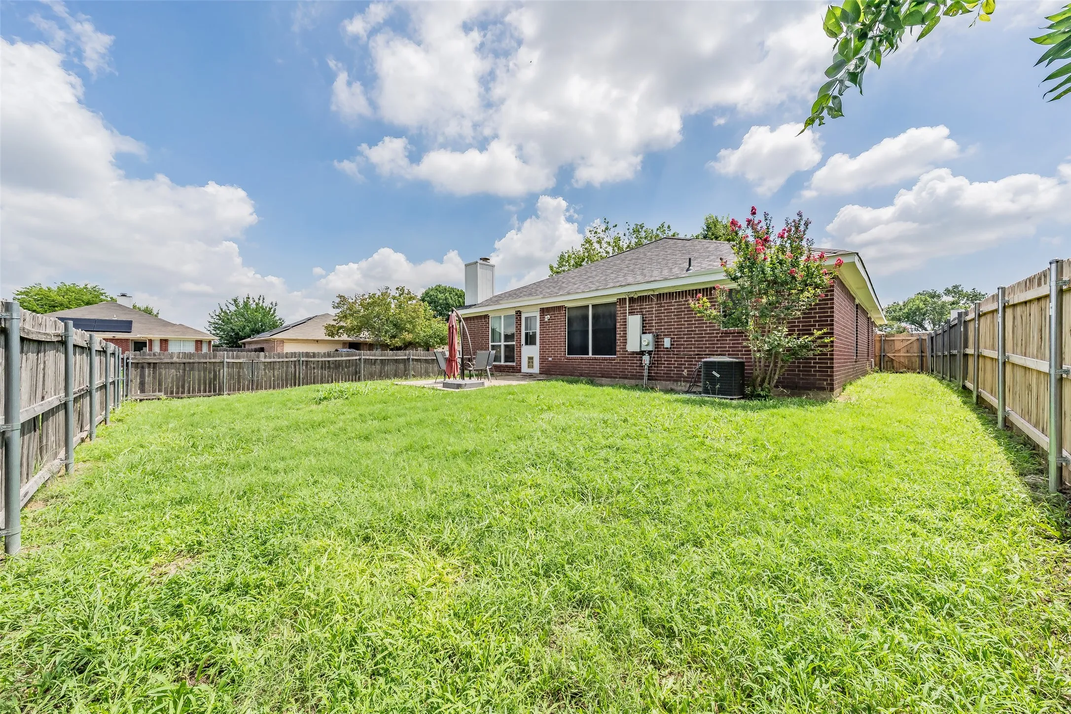 Expansive backyard featuring a large grass area, wood privacy fencing, and a brick exterior home with a patio