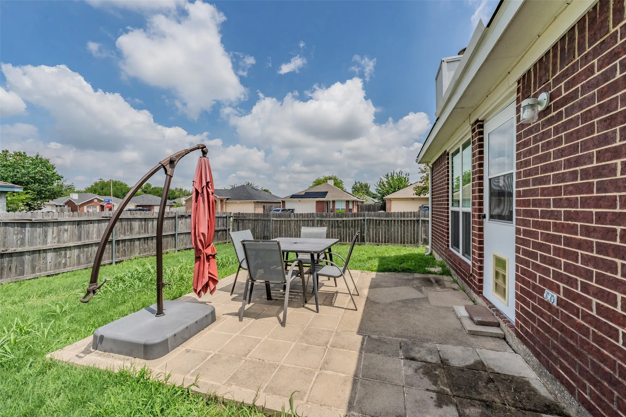 Private backyard featuring a paved patio area, brick exterior, multiple windows, and a wood privacy fence