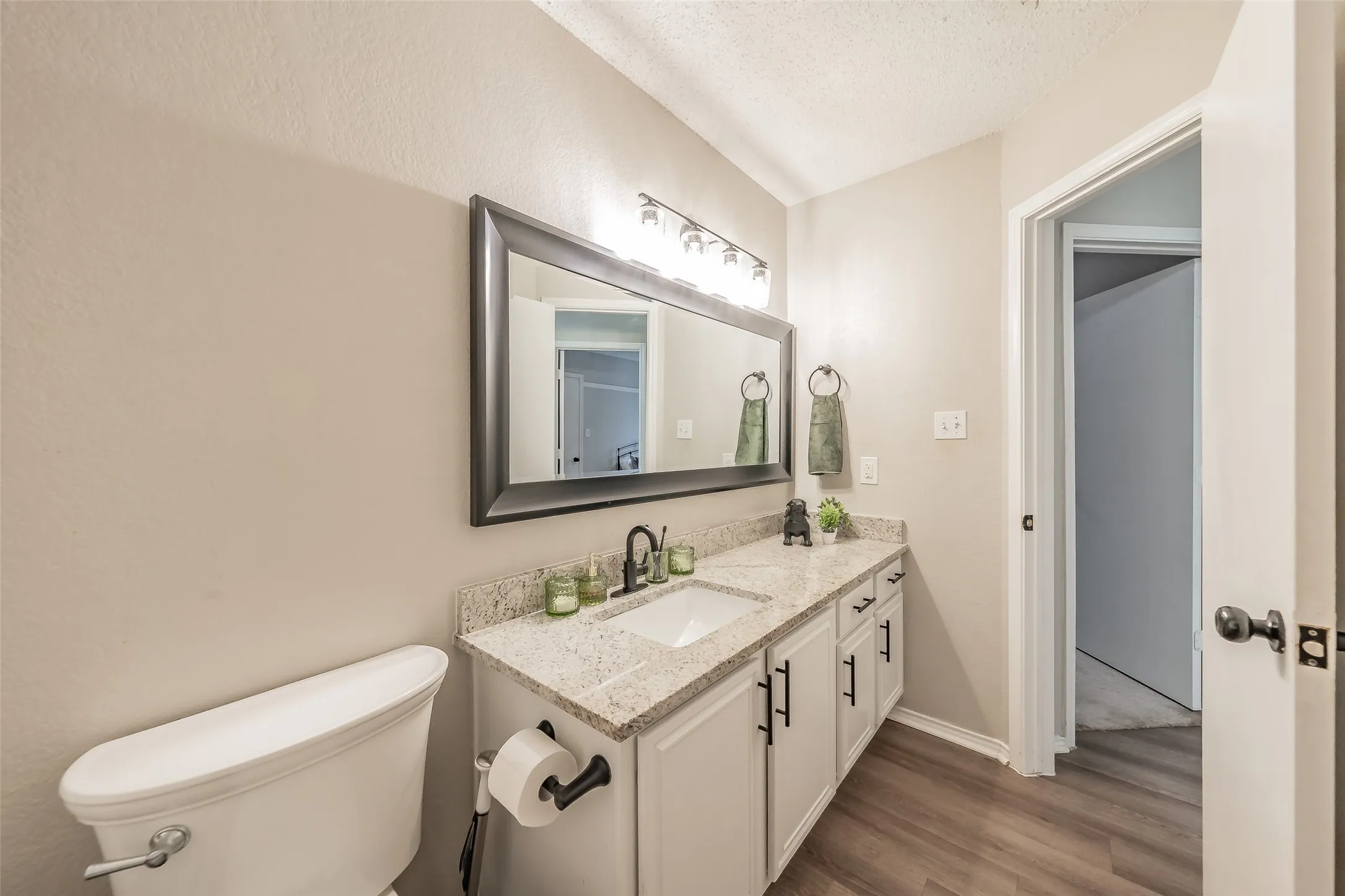 Bathroom vanity featuring a single sink, light-toned countertop, white cabinetry with dark hardware, and a framed mirror with overhead lighting