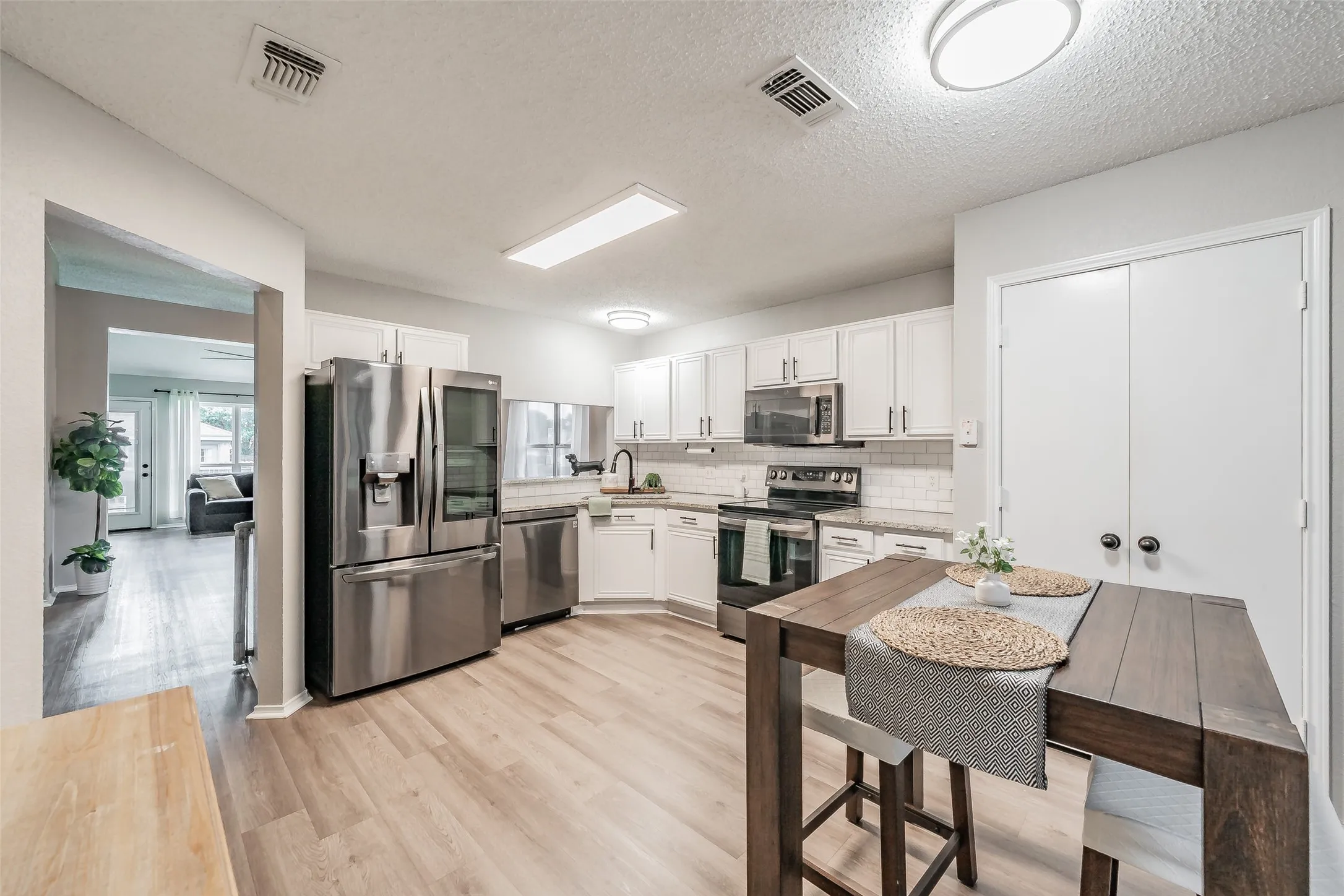 Kitchen featuring stainless steel appliances, white cabinetry, light wood-finish flooring, white subway tile backsplash, and recessed lighting