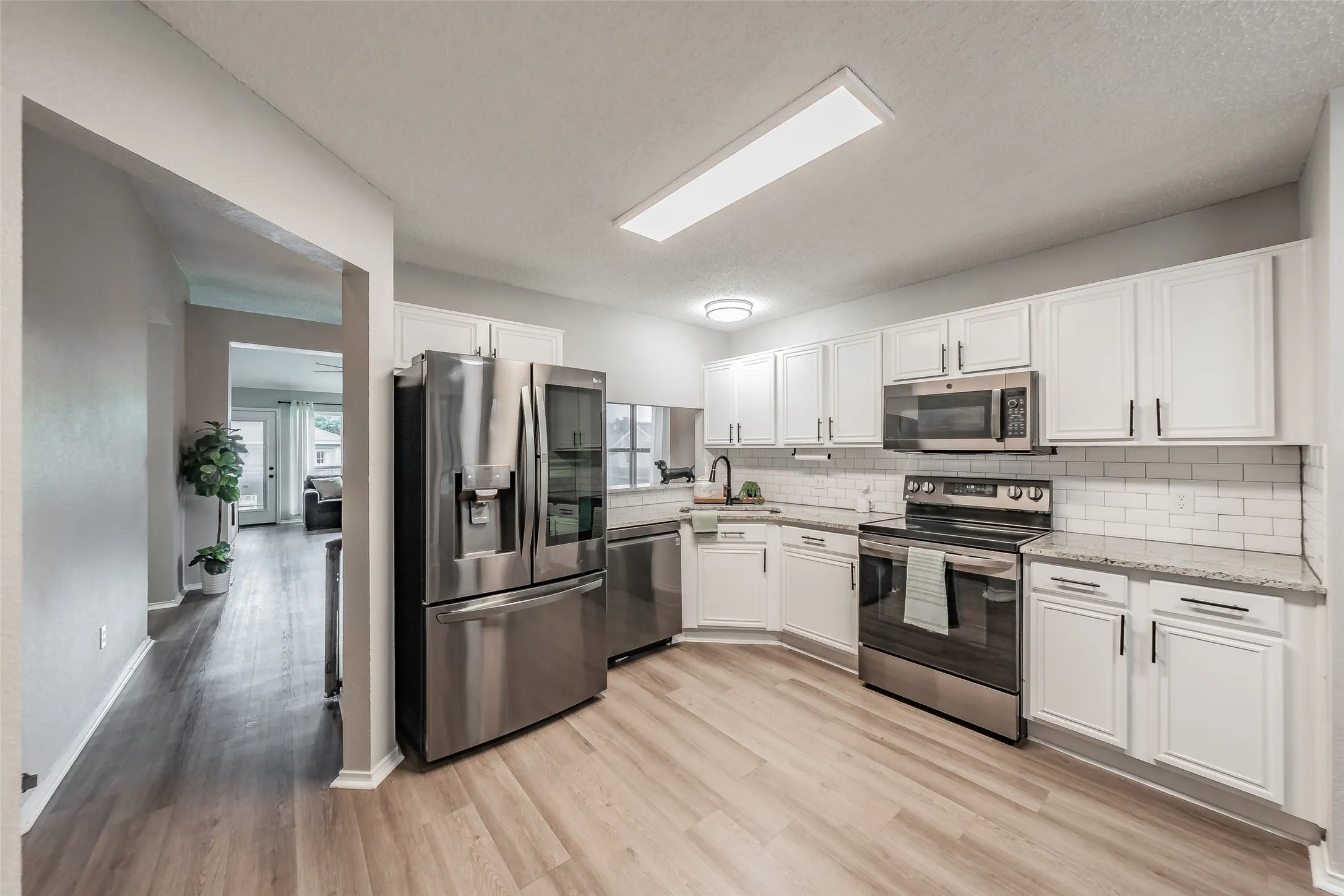 Modern kitchen featuring white cabinetry, stainless steel appliances, light granite-style countertops, and subway tile backsplash