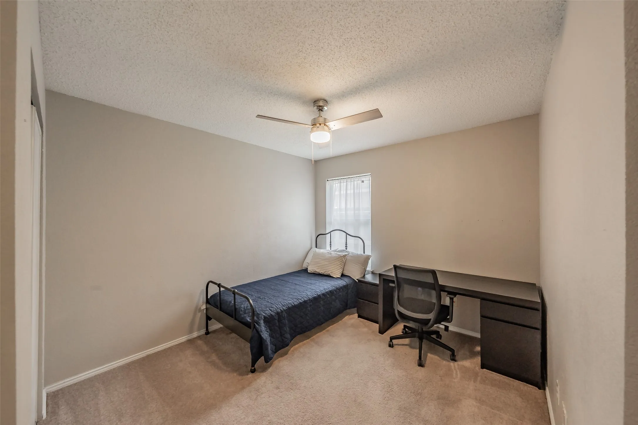 Neutral-toned room with carpet flooring, a window with sheer curtains, and a ceiling fan with integrated lighting