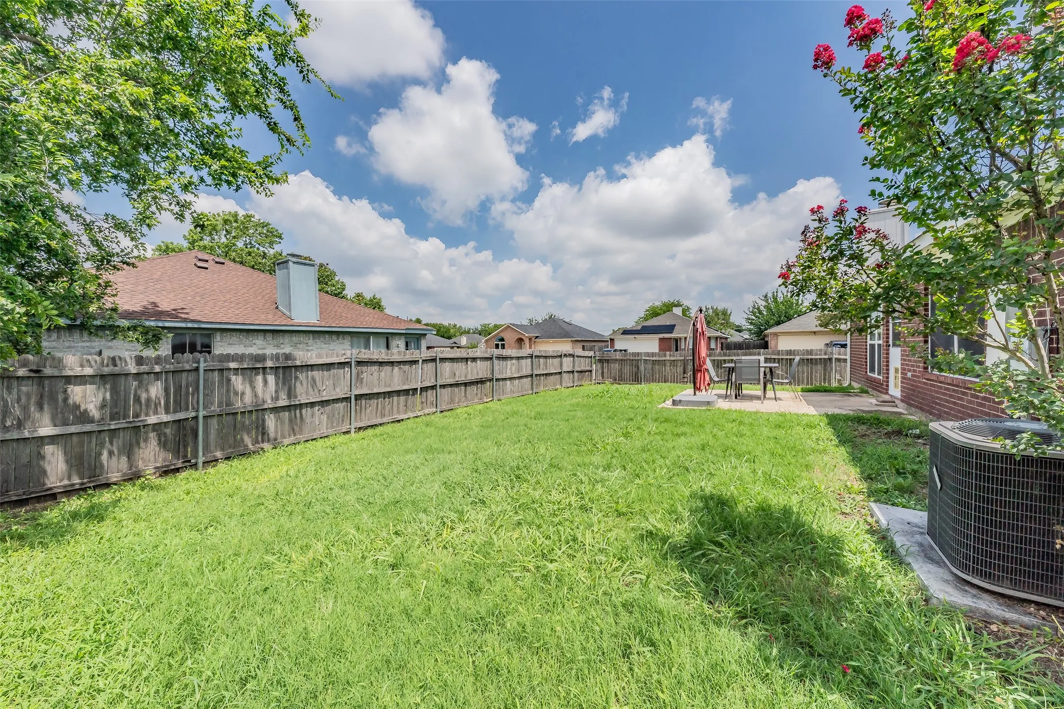 Expansive backyard featuring a large grass area, wood privacy fencing, and a concrete patio