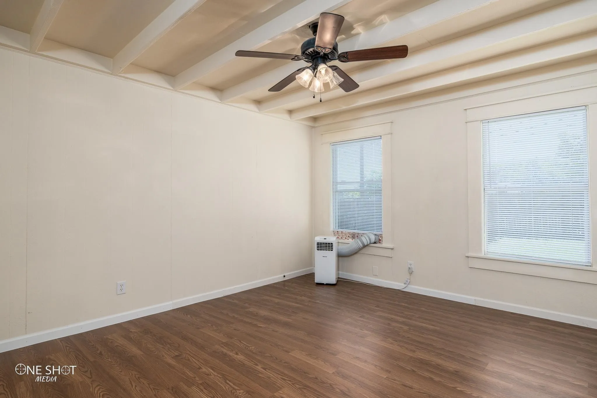 Empty room with beam ceiling, ceiling fan, and dark hardwood / wood-style flooring