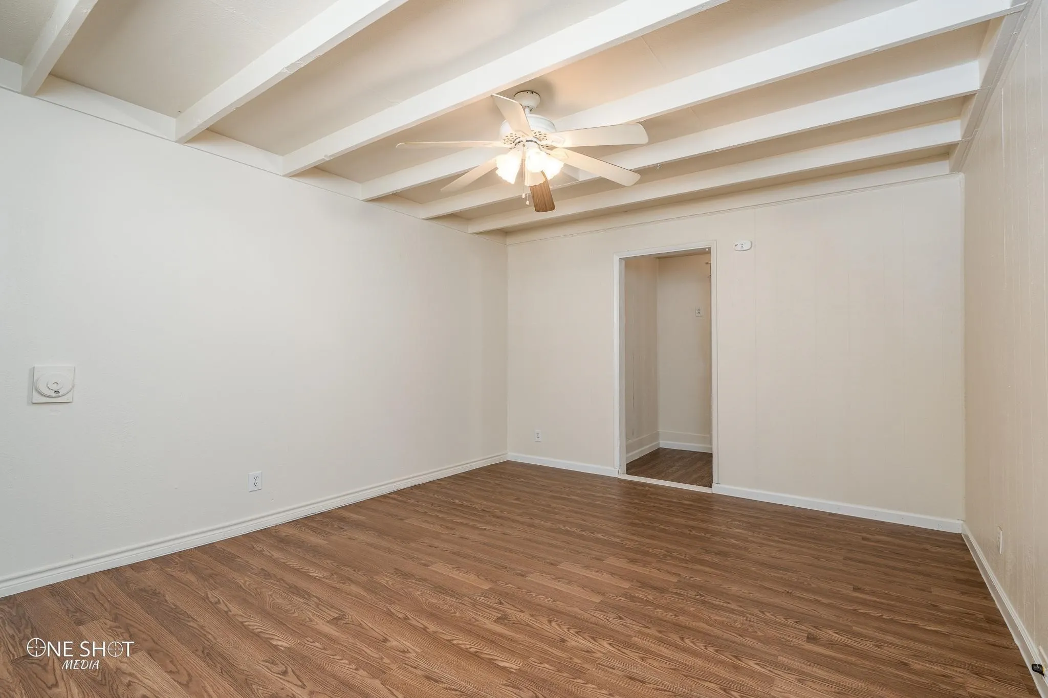 Empty room with beamed ceiling, hardwood / wood-style flooring, and ceiling fan