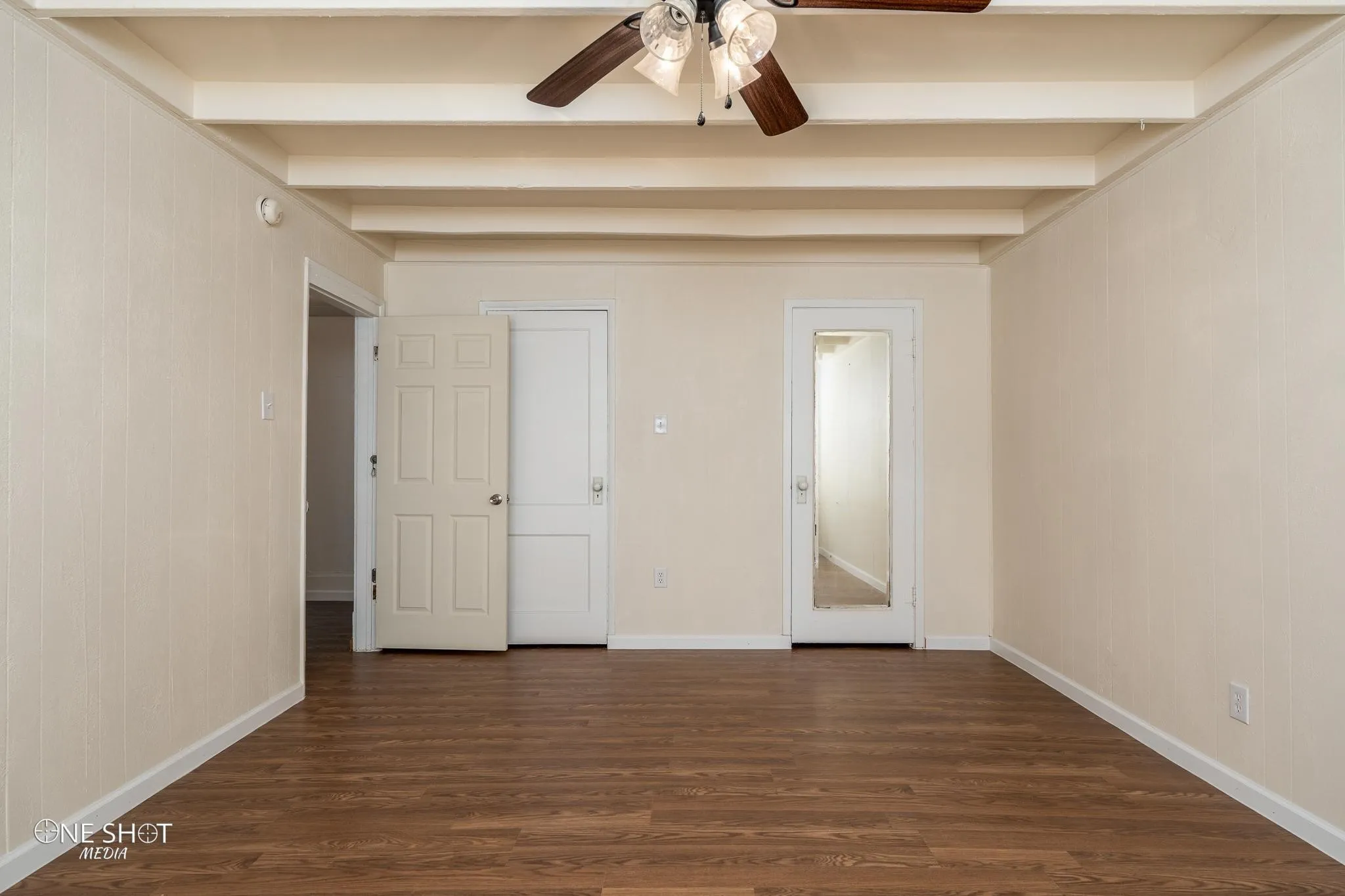Unfurnished room featuring beam ceiling, ceiling fan, and dark wood-type flooring