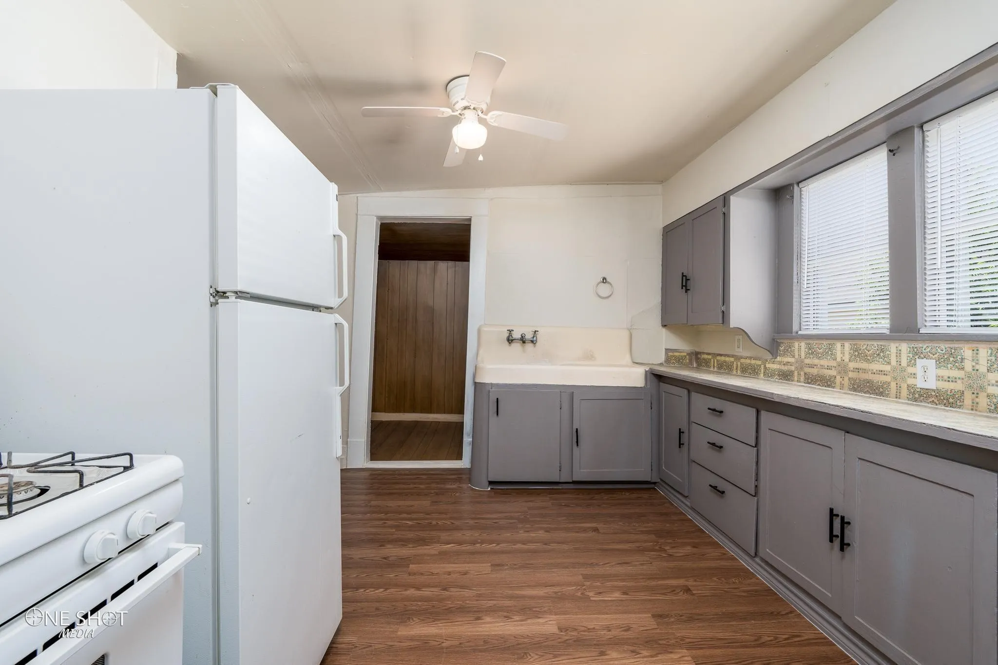 Kitchen featuring a wealth of natural light, dark wood-type flooring, gray cabinetry, backsplash, and ceiling fan