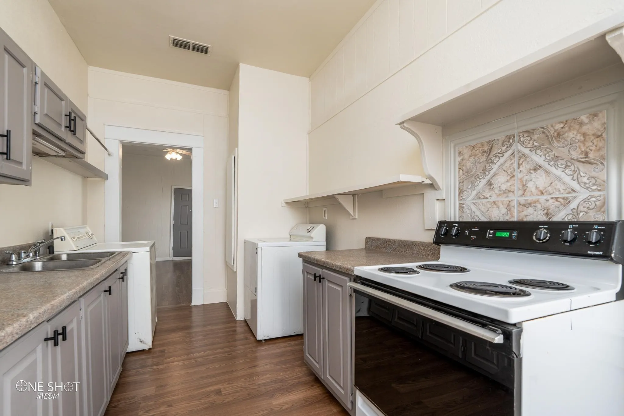 Kitchen featuring dark wood-type flooring, gray cabinetry, white electric range oven, sink, and washing machine and dryer