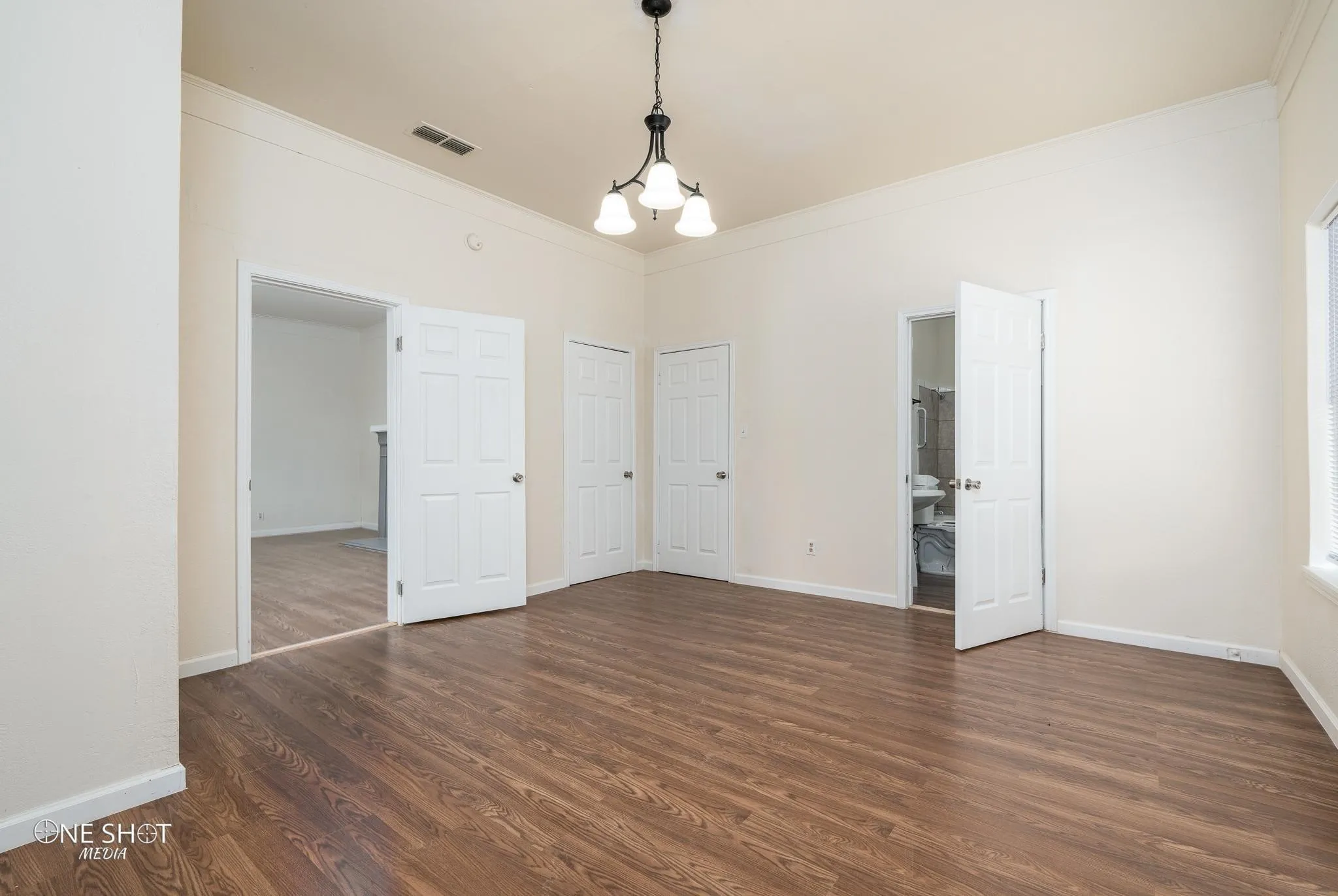 Unfurnished bedroom featuring ornamental molding, dark hardwood / wood-style floors, connected bathroom, and an inviting chandelier