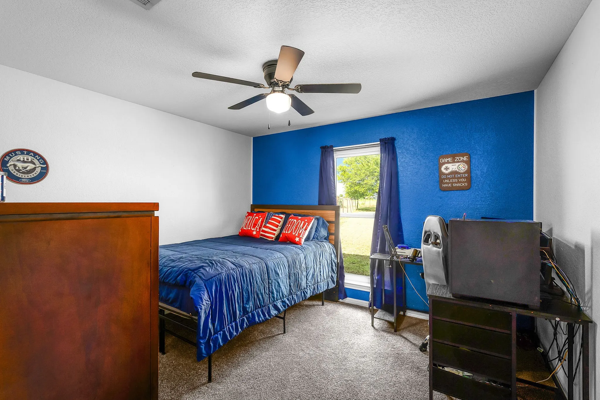 Room featuring contrasting white and blue painted walls, a ceiling fan with integrated lighting, a window with exterior views, and neutral-toned carpeting