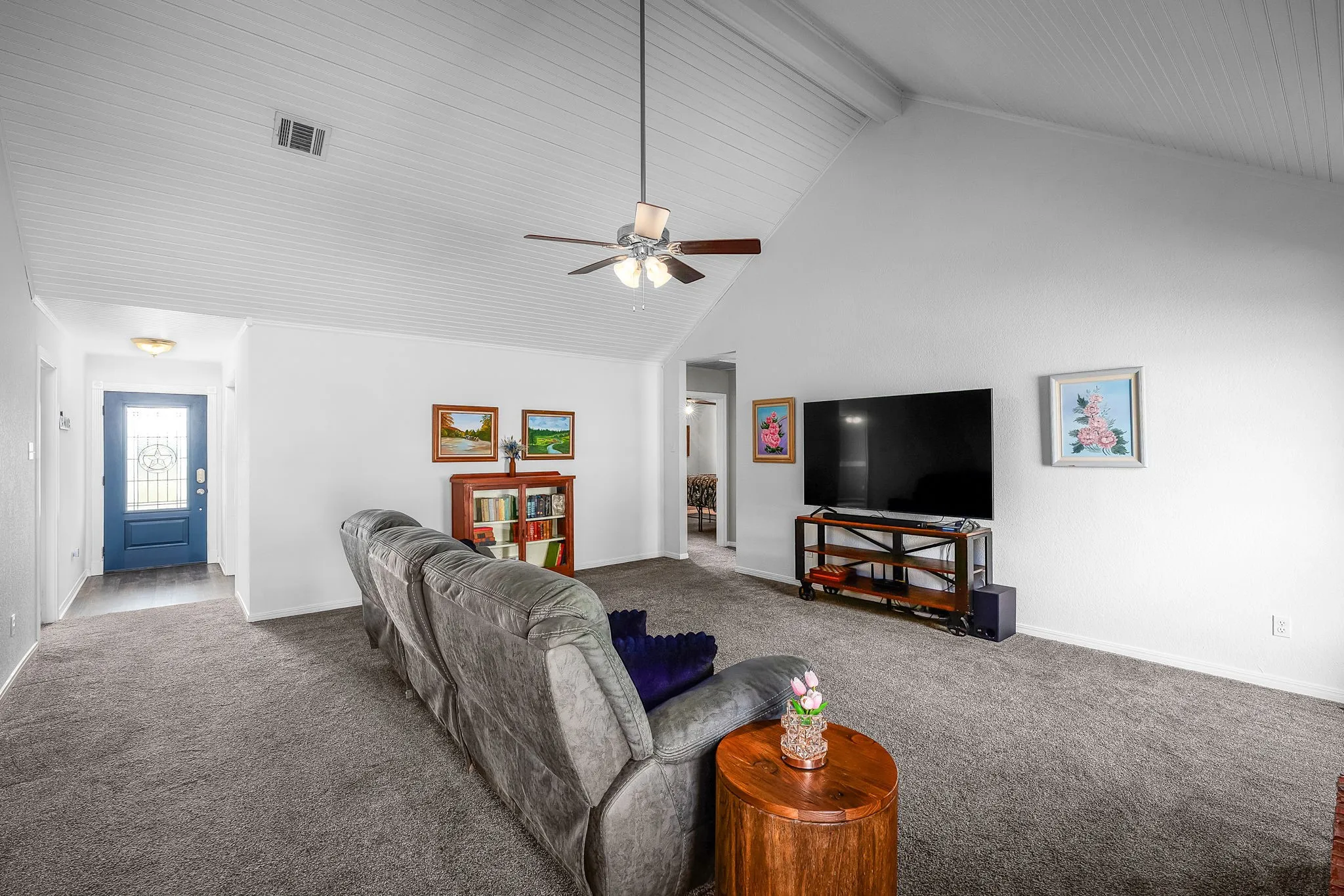 Spacious living area featuring a vaulted shiplap ceiling, ceiling fan, and grey carpeting