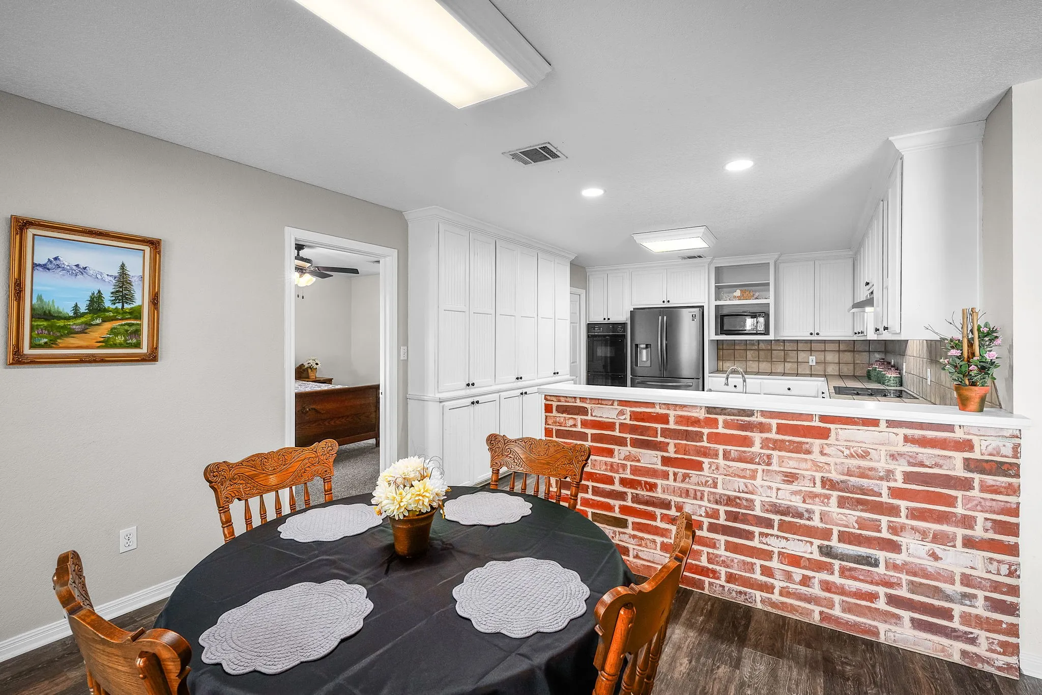 Kitchen and dining area featuring a brick accent wall, white cabinetry, integrated appliances, and wood-finish flooring