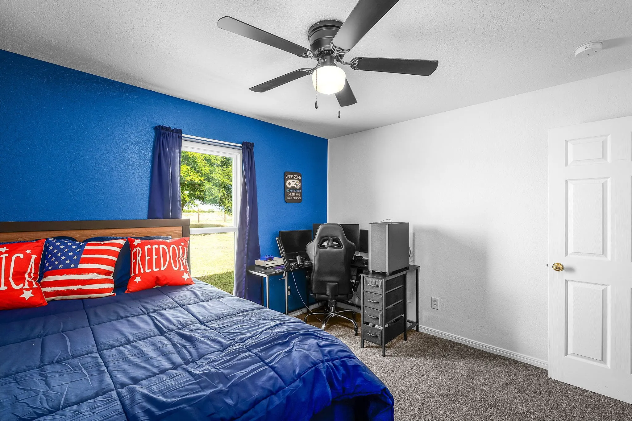 Bedroom featuring neutral carpeting, a blue accent wall, a multi-pane window, a ceiling fan with integrated lighting, and a paneled white door