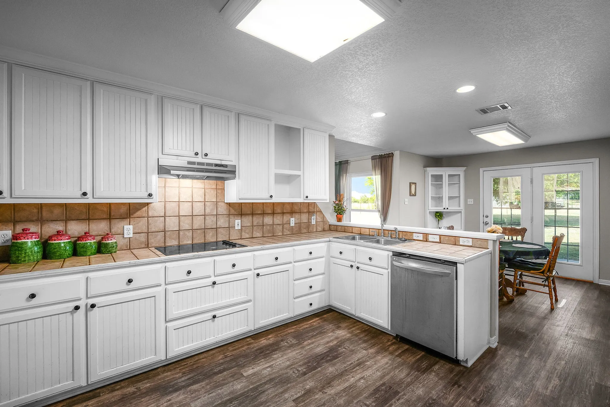 Kitchen featuring white cabinetry, tile backsplash, built-in cooktop, stainless steel dishwasher, and wood-finish flooring